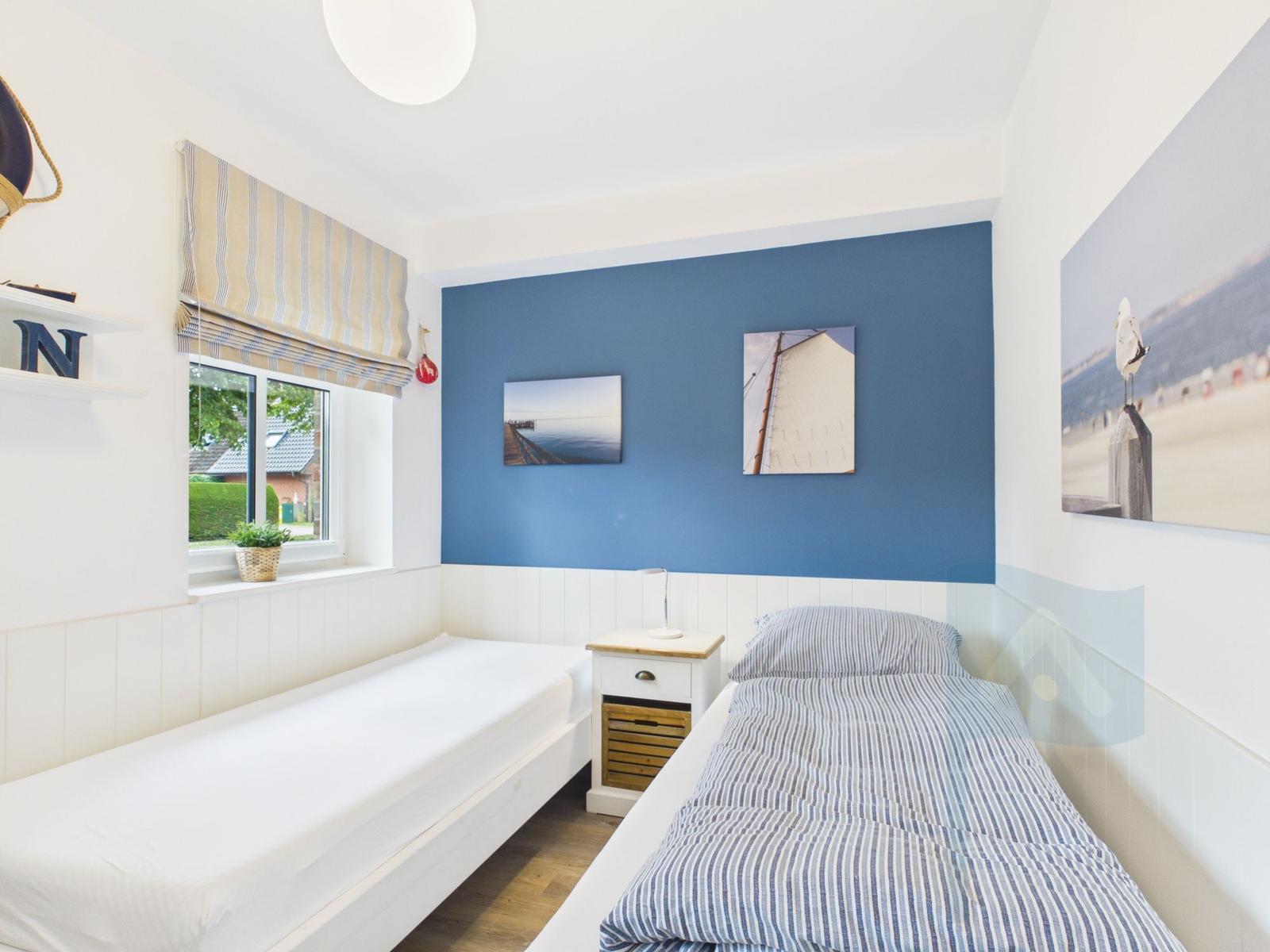 Zimmer mit zwei Betten, blauer Wand und Meeresbildern.