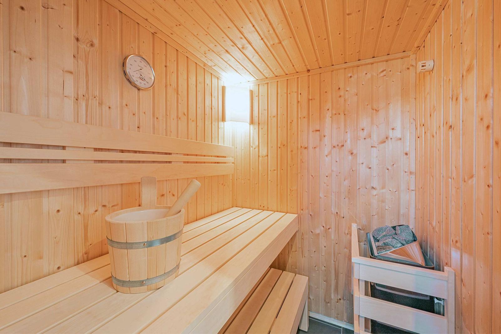 Sauna mit Holzbank, Eimer und Thermometer an der Wand.