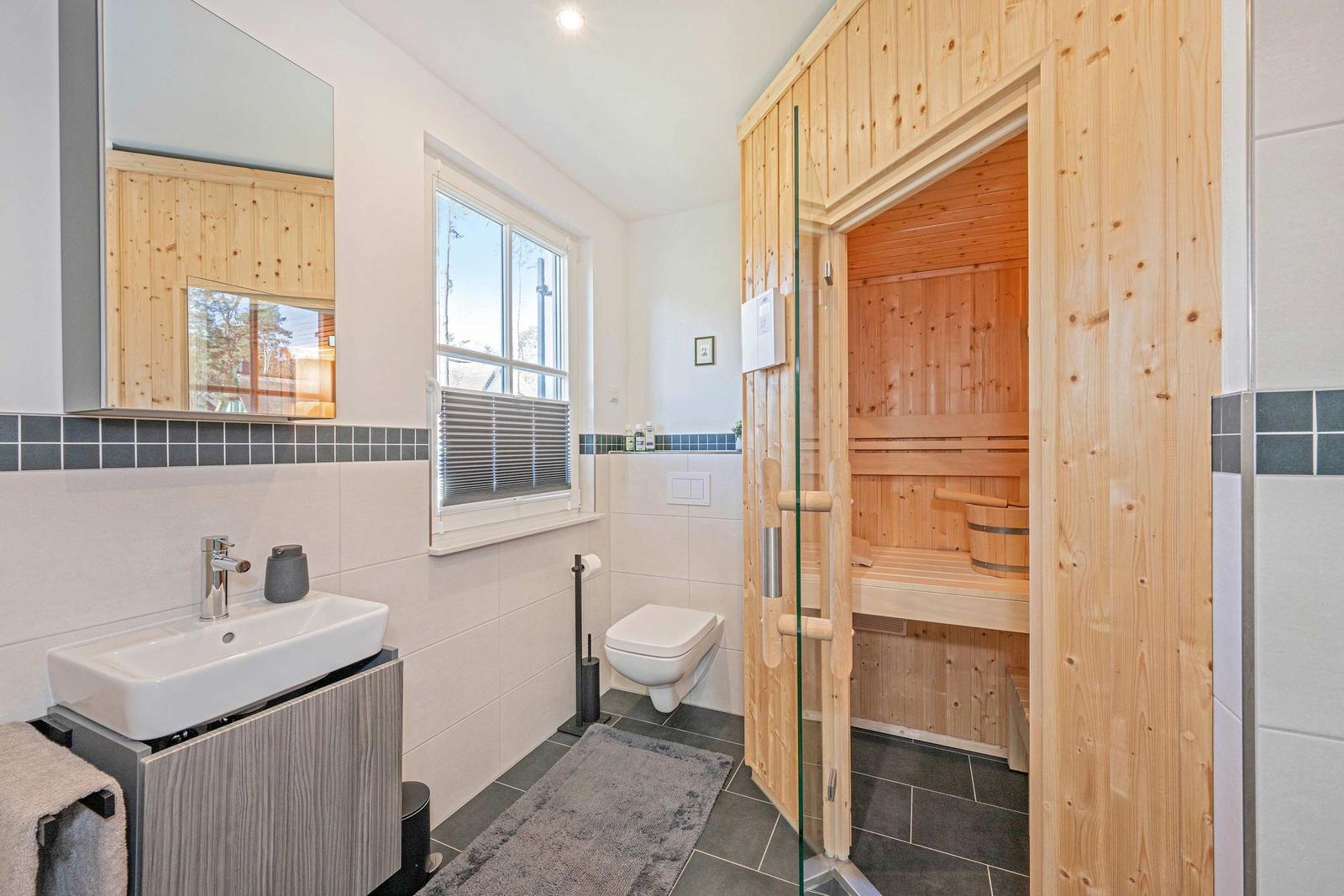 Badezimmer mit Sauna, Waschbecken und Toilette. Holzverkleidung und Fenster sichtbar.