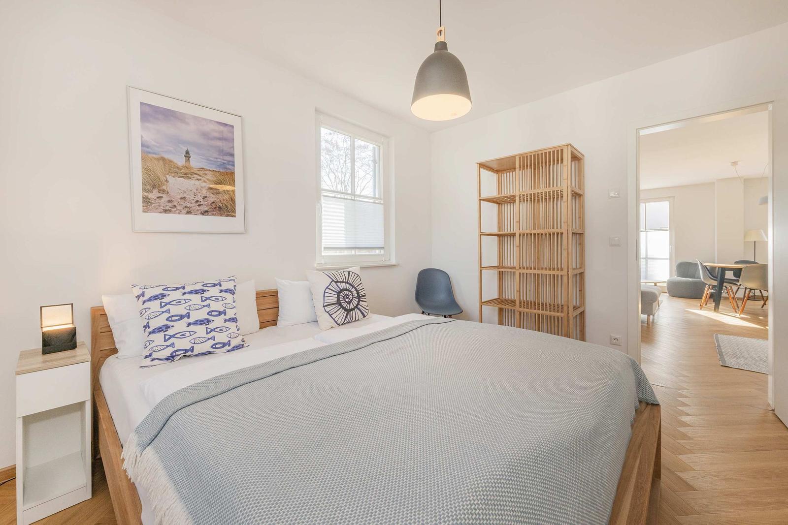 Schlafzimmer mit Bett, Nachttisch, Wandbild und Blick in Wohnbereich.