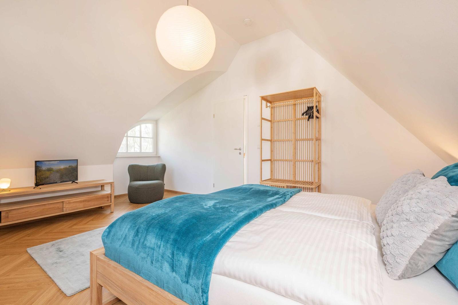 Schlafzimmer mit Bett, Kleiderschrank und Fernseher unter Dachschrägen.