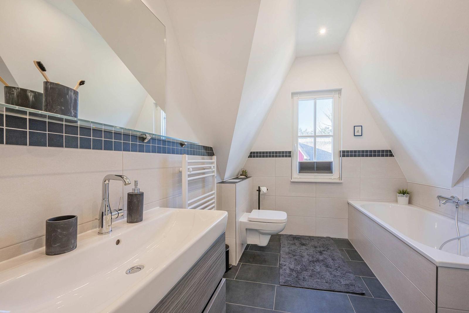 Badezimmer mit Dusche, Badewanne und Fenster unter Dachschrägen.