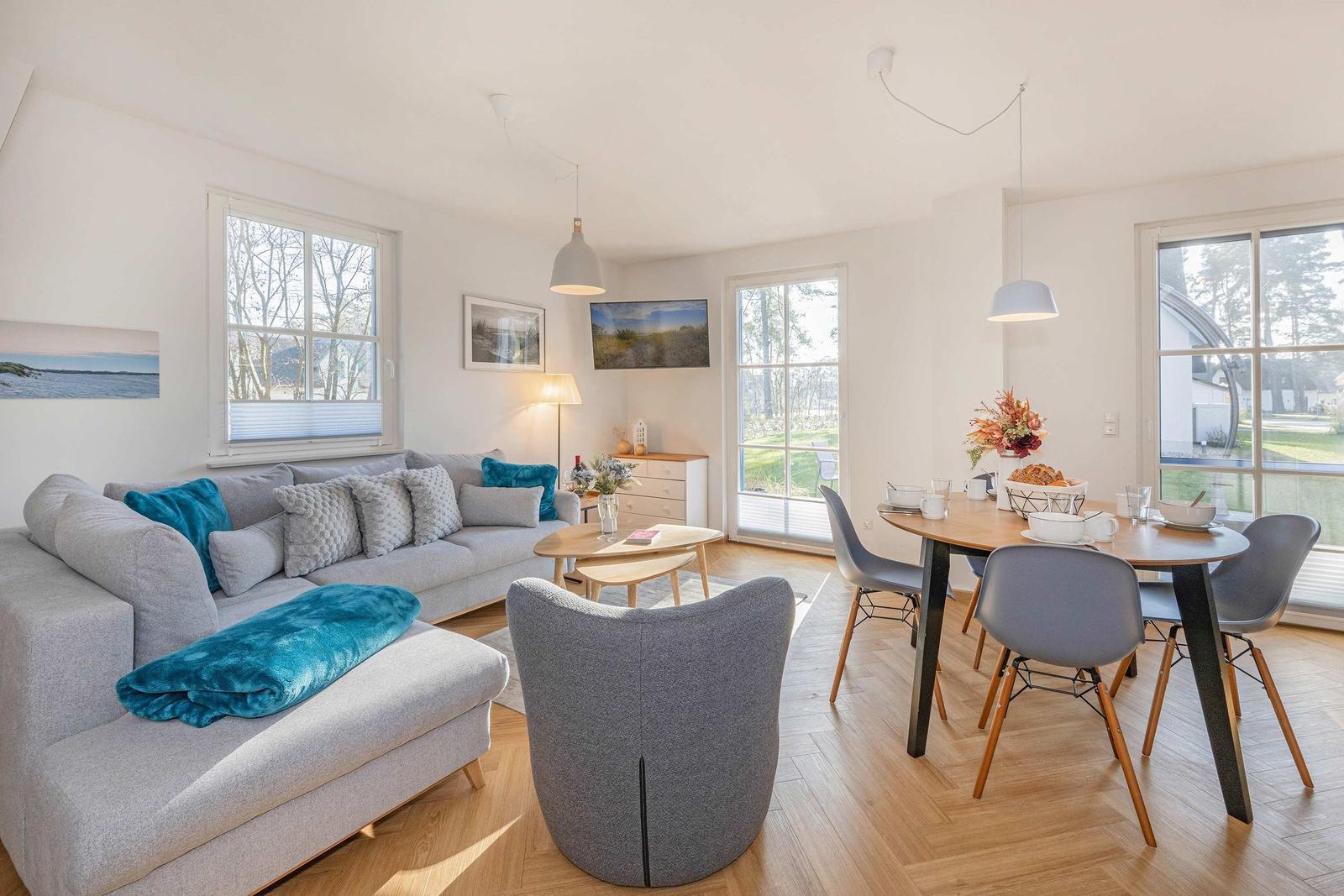 Wohn- und Essbereich mit Sofa, Tisch und Stühlen. Holzboden und große Fenster.