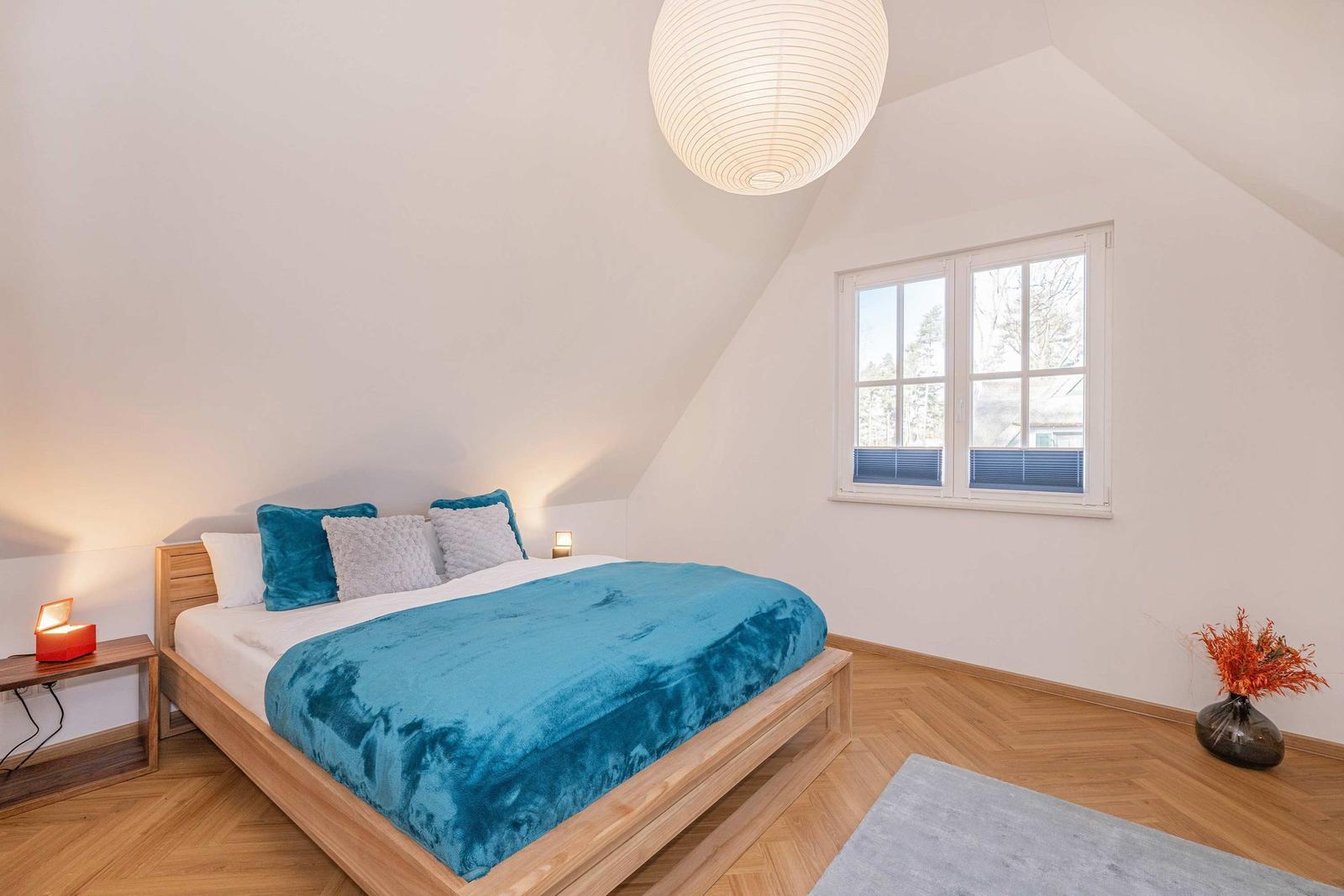 Schlafzimmer mit Holzbett, blauer Decke, Fenster und Deckenlampe.