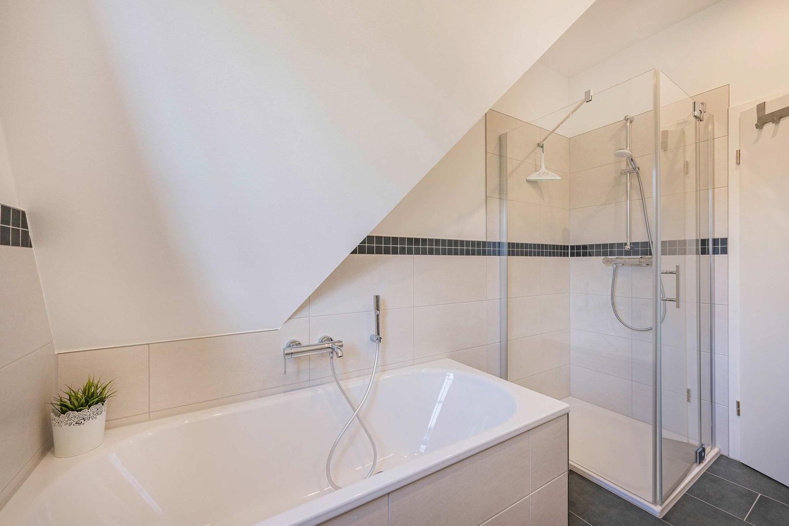 Badezimmer mit Badewanne und Dusche unter schräger Decke.