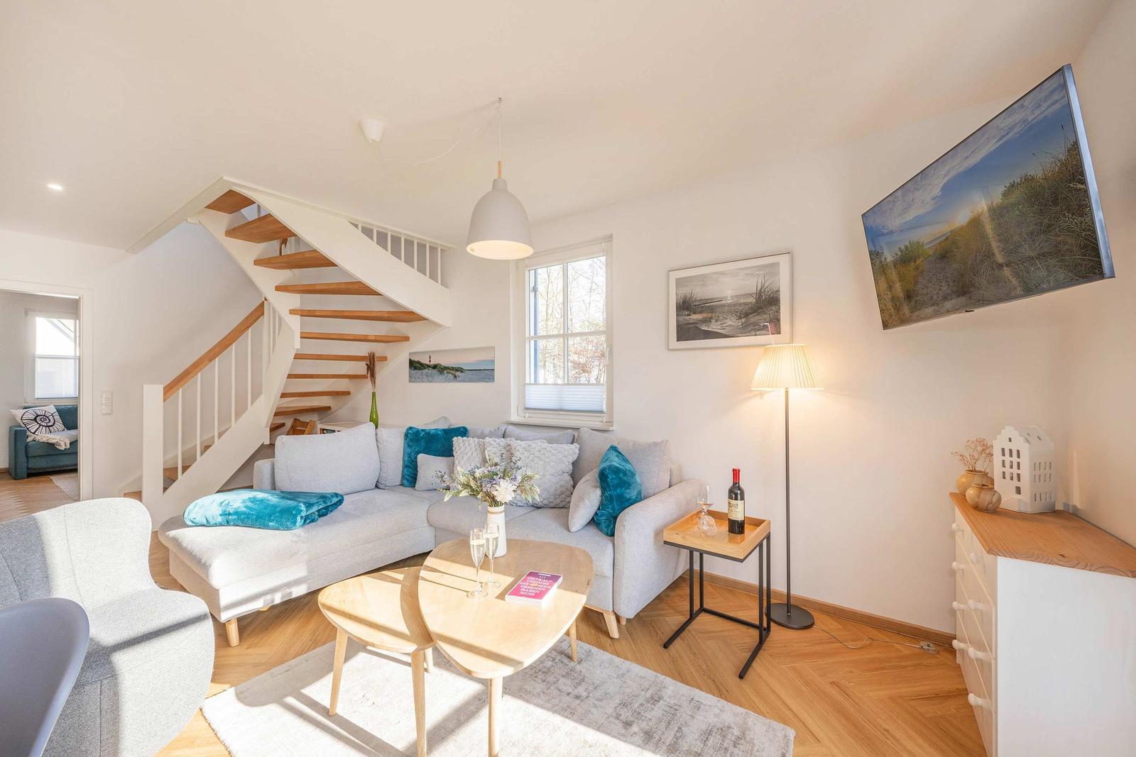 Wohnzimmer mit Sofa, Tisch und Treppenhaus. Wandbild und Fernseher an der Wand.