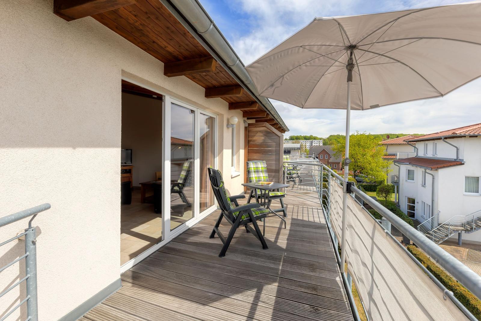 Terrasse mit Sonnenschirm und Gartenmöbeln. Blick auf Wohnhäuser und Grünflächen.