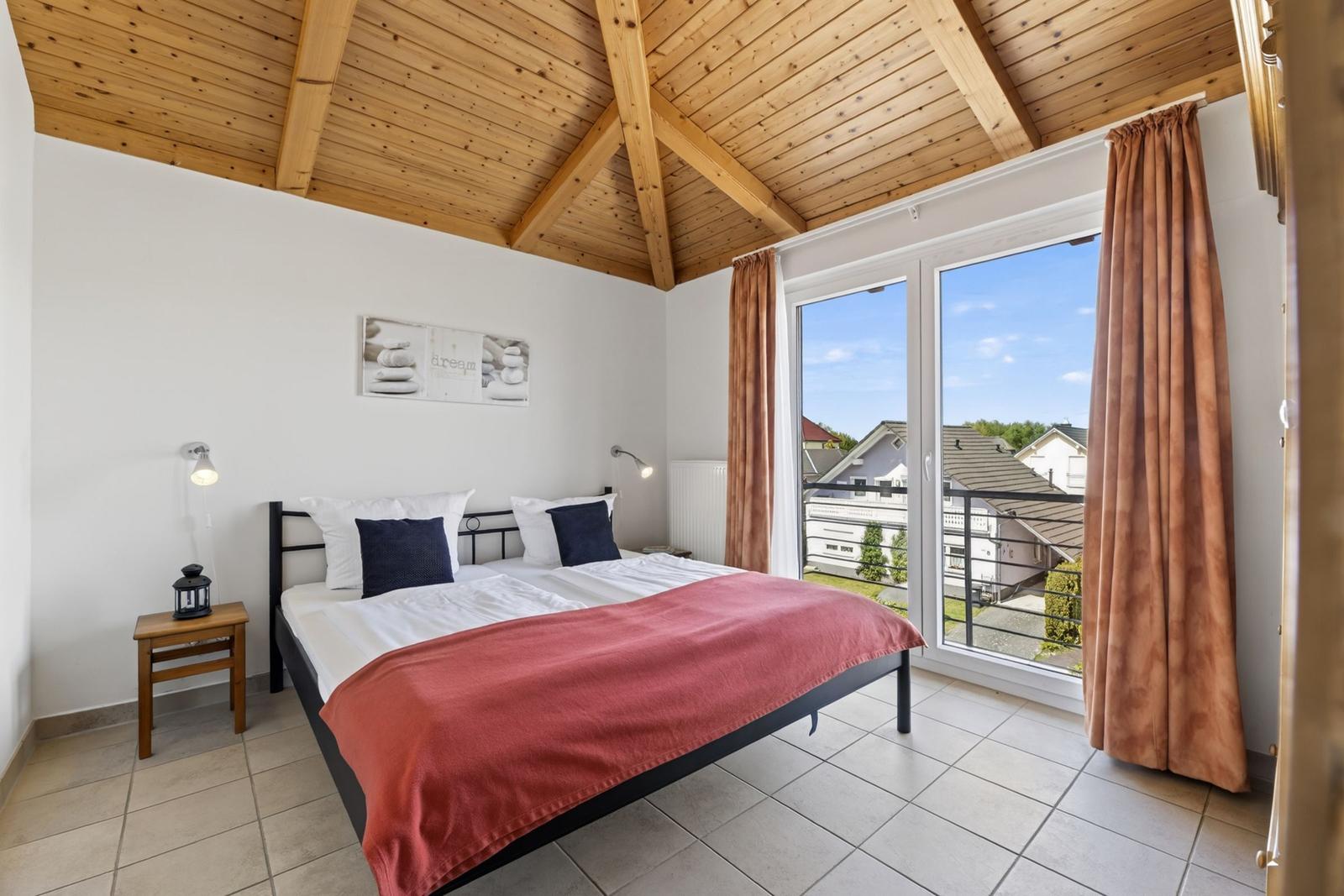 Schlafzimmer mit Doppelbett, Holzdecke und Balkonansicht.