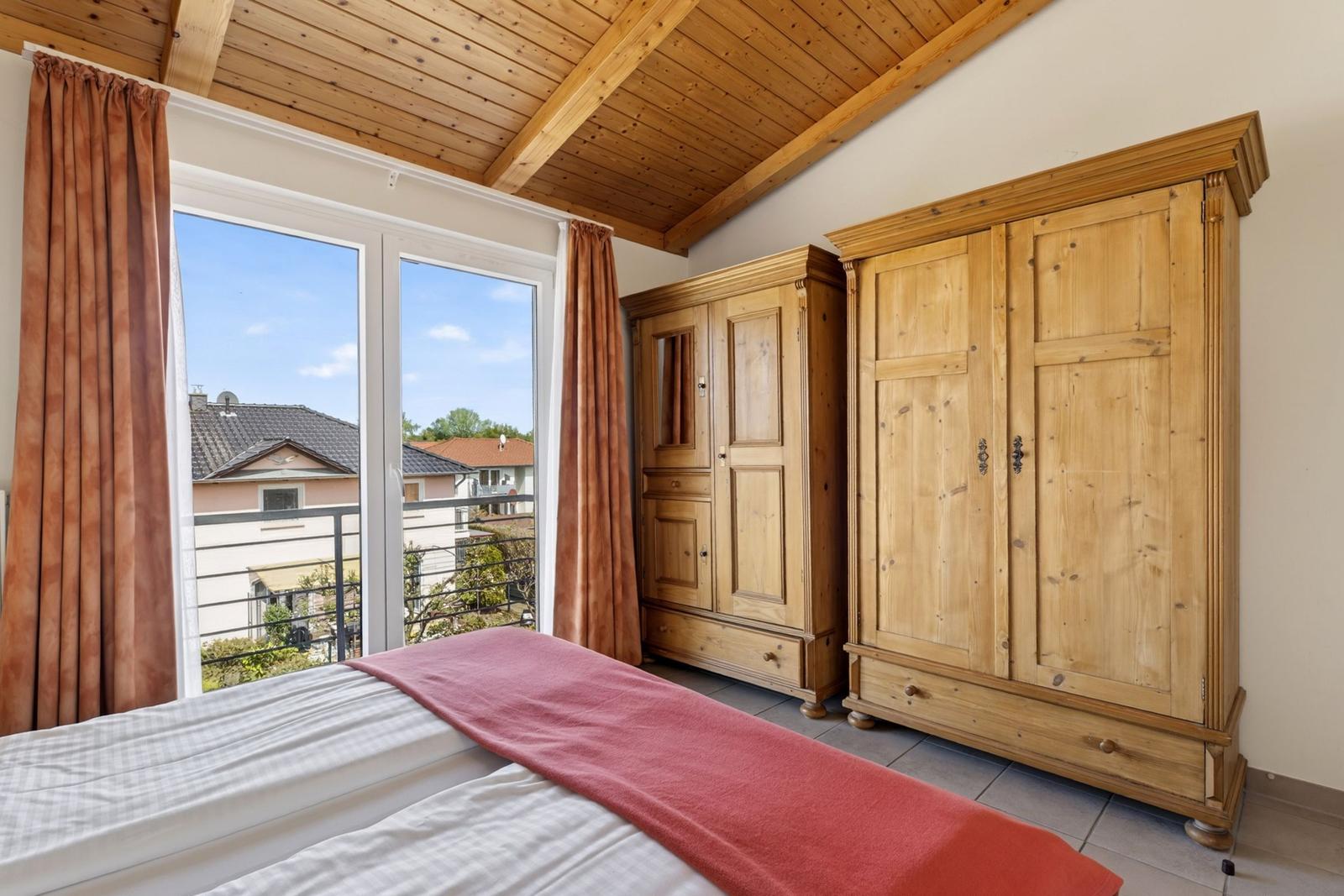 Schlafzimmer mit Holzboden, großen Fenstern und zwei Holzschranken.