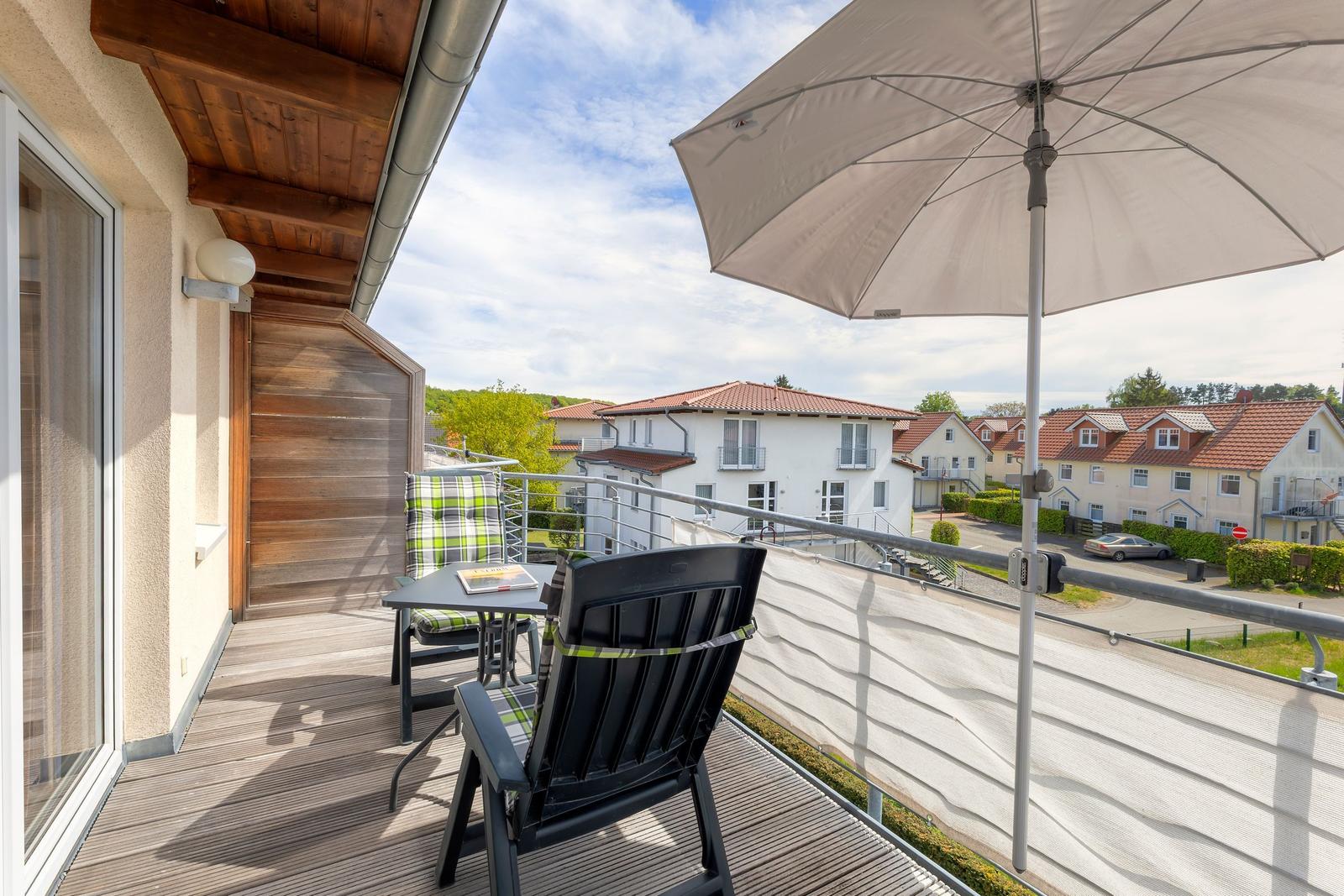 Terrasse mit Tisch, Stühlen und Sonnenschirm. Blick auf Wohnhäuser und Grünanlagen.