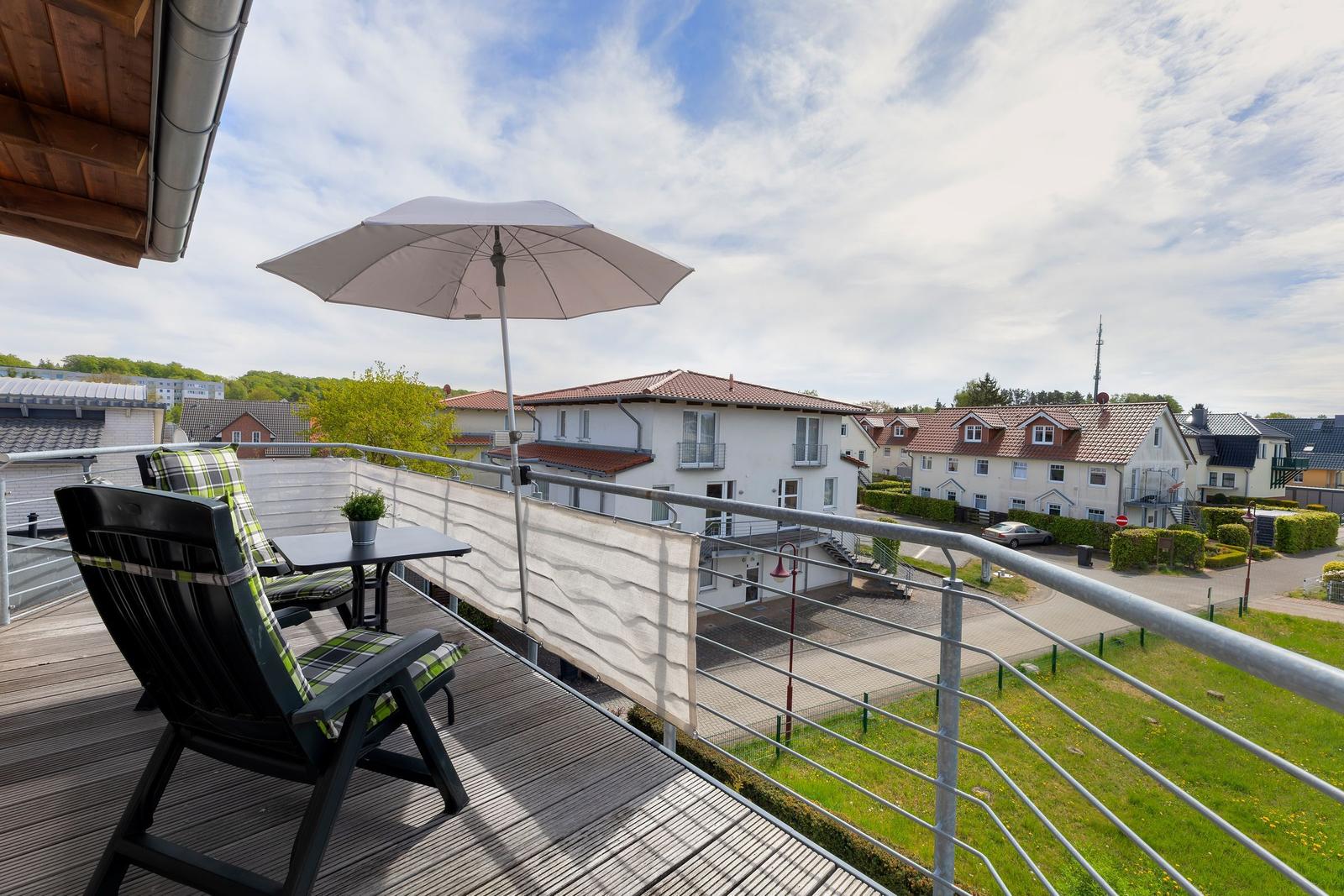 Terrasse mit Sitzgruppe, Sonnenschirm und Blick auf Wohnhäuser und Grünflächen.