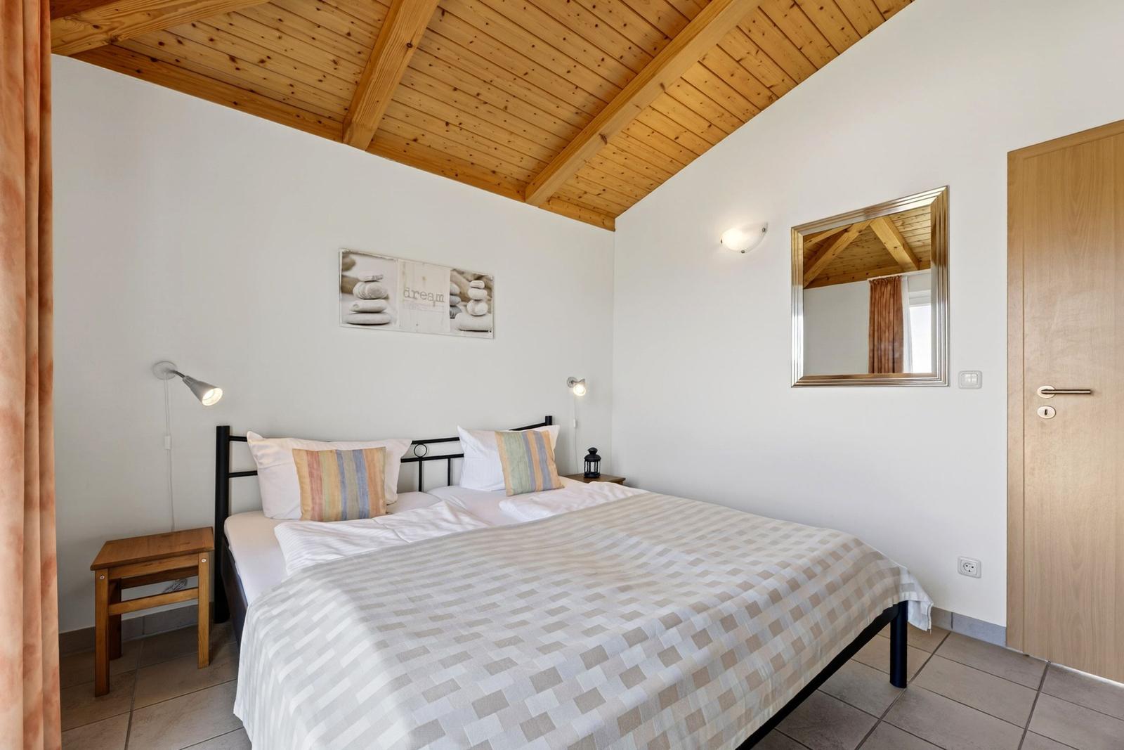 Schlafzimmer mit Bett, Spiegel und Holzdecke.