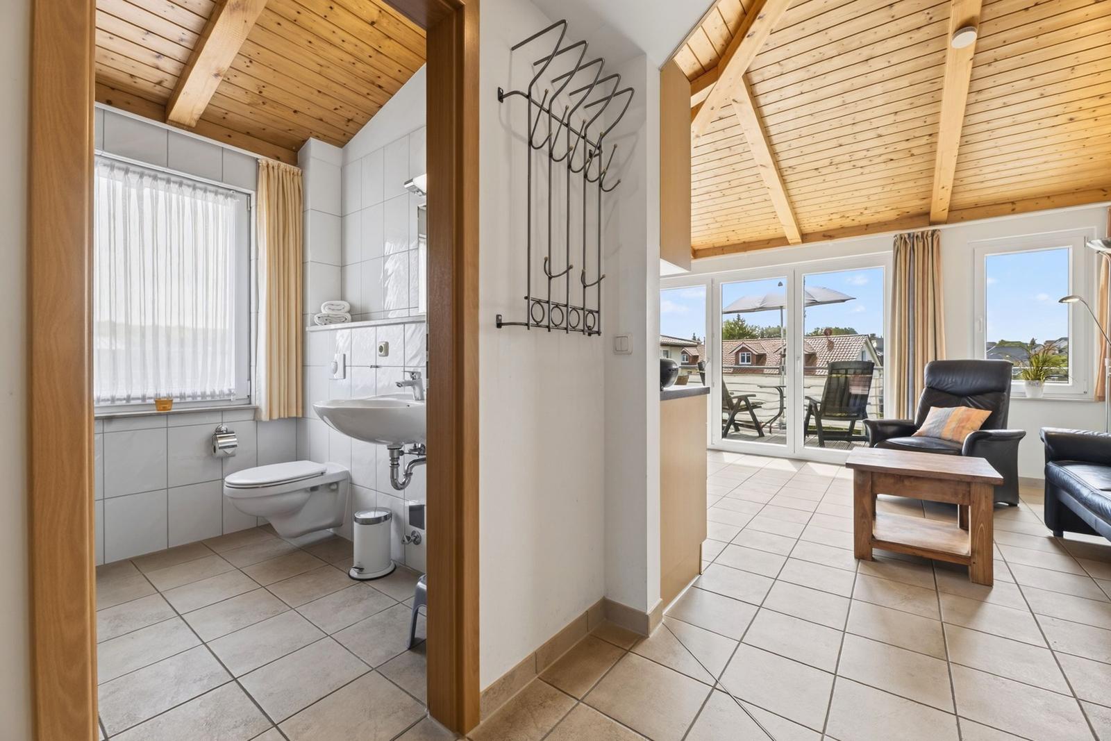Badezimmer mit Toilette und Waschbecken. Wohnbereich mit Sitzgelegenheiten und Balkonansicht.