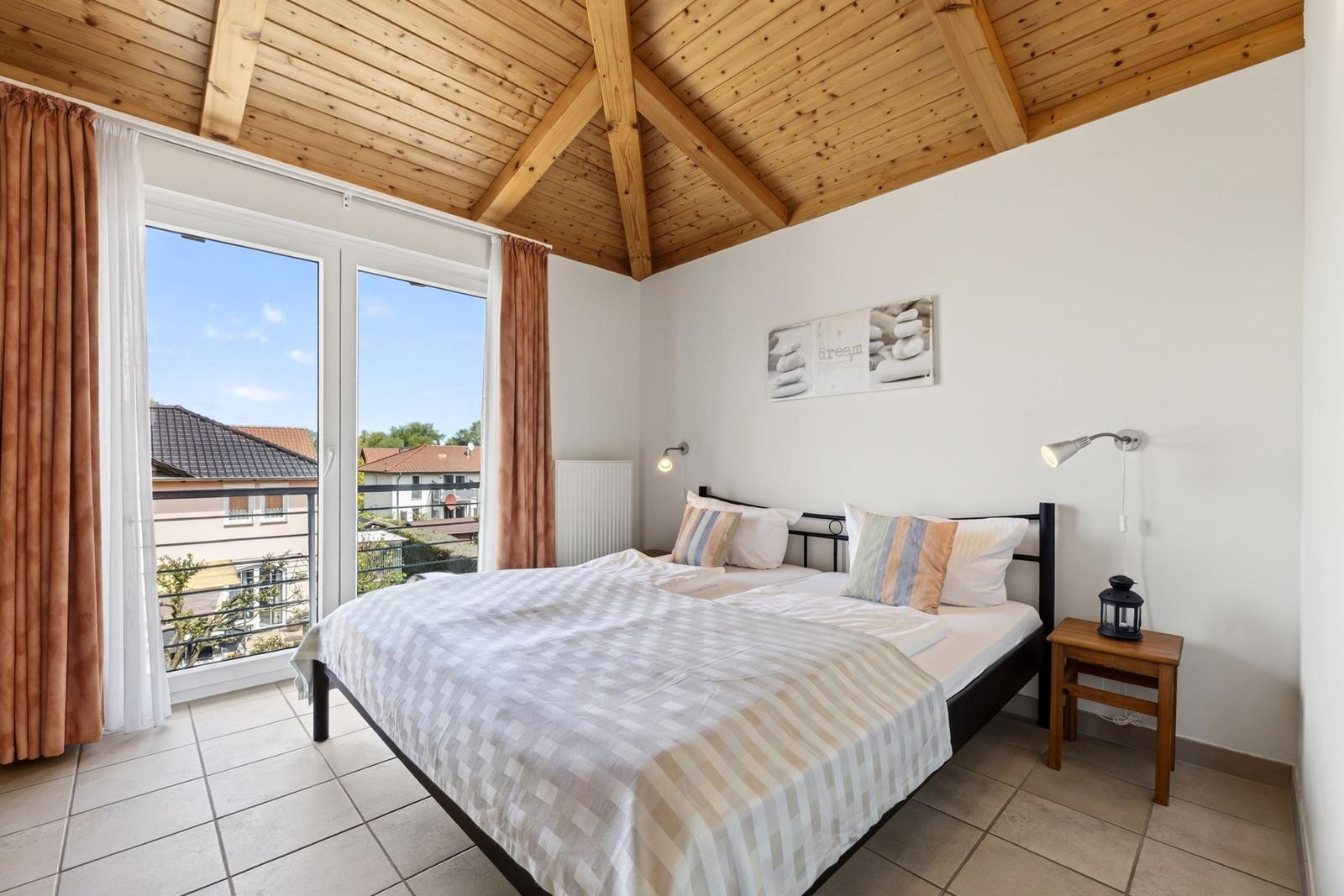 Schlafzimmer mit Balkon, Holzdecke und Bett mit Kissen.