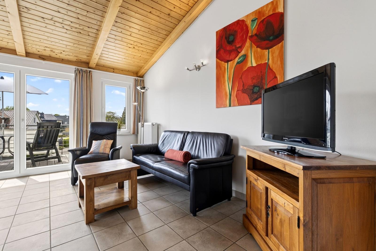 Wohnzimmer mit Sofa, Sessel, Fernseher und Blick auf die Terrasse.