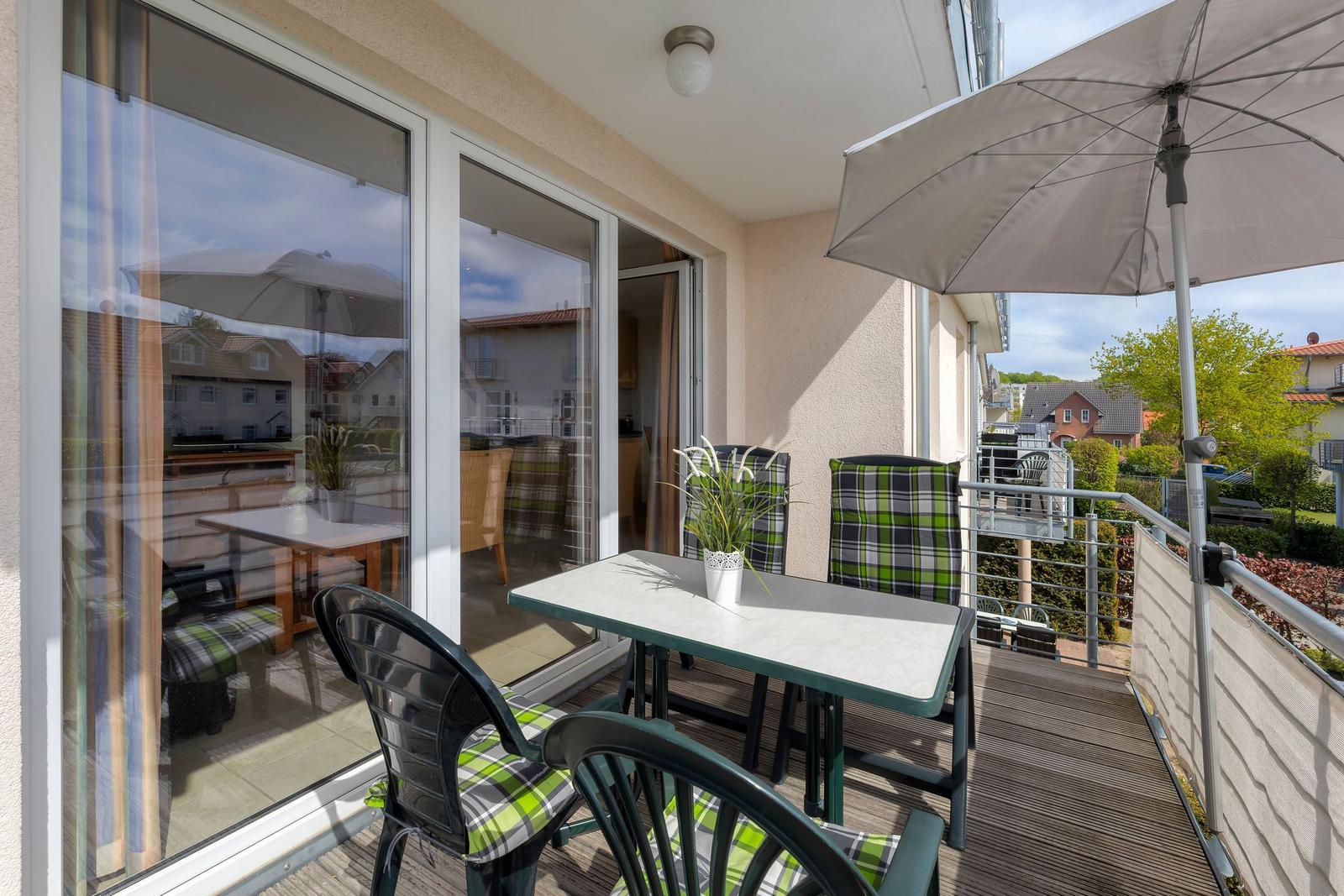 Terrasse mit Tisch, Stühlen und Sonnenschutz. Blick auf Wohngebiet mit Bäumen.