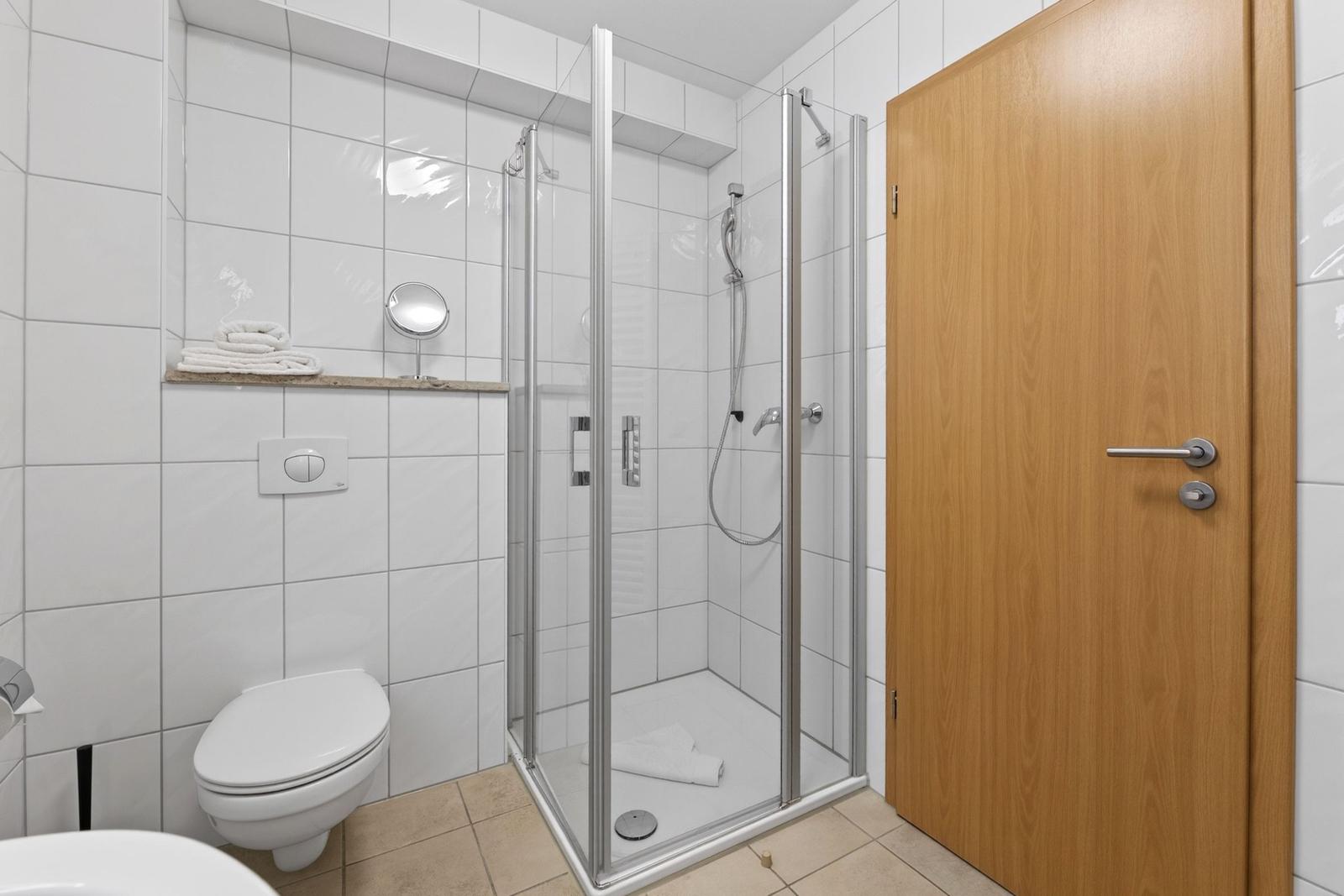Badezimmer mit Dusche, Toilette und Spiegelfläche an der Wand.