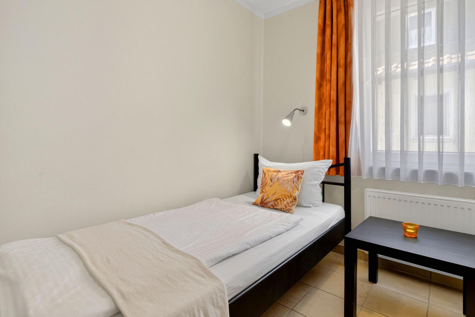 Ein Schlafzimmer mit Einzelbett, Fenster mit Vorhängen und kleinem Tisch.