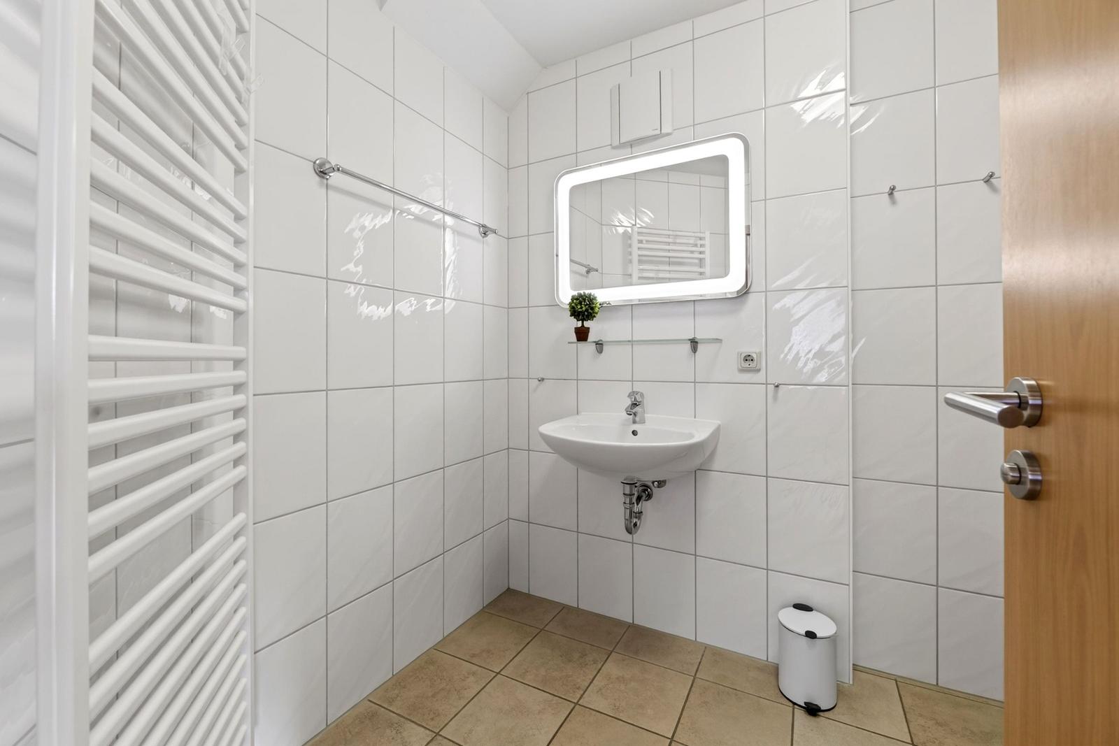 Badezimmer mit Waschbecken, Spiegel, Heizung und Mülleimer.