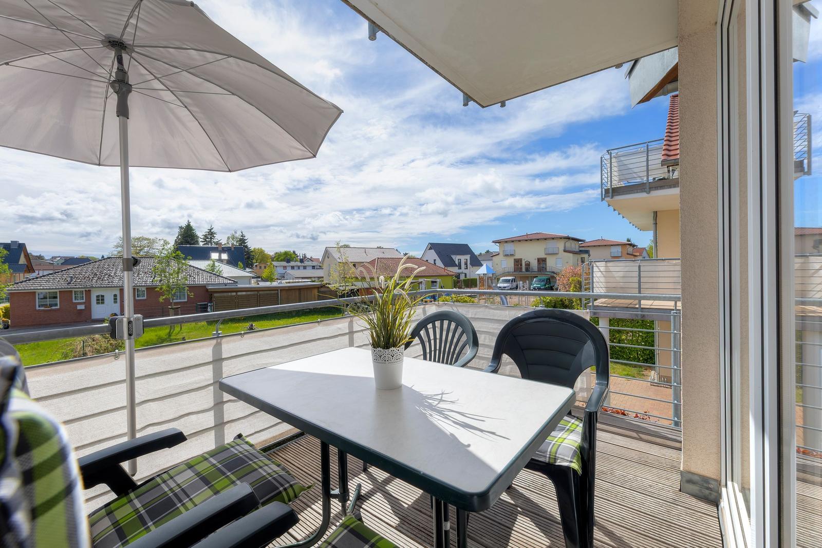 Terrasse mit Tisch, Stühlen und Sonnenschirm. Blick auf Wohngebiet mit Häusern und Grünflächen.