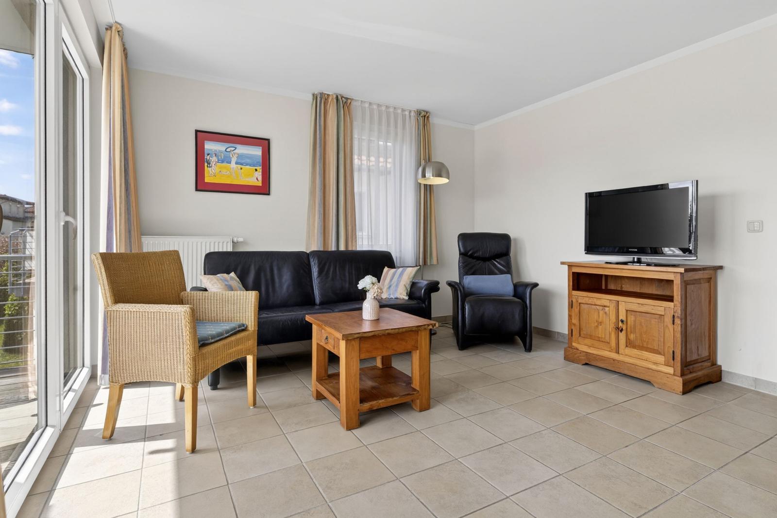 Wohnzimmer mit Sofa, Sessel, Couchtisch und Fernseher auf Holzboard.
