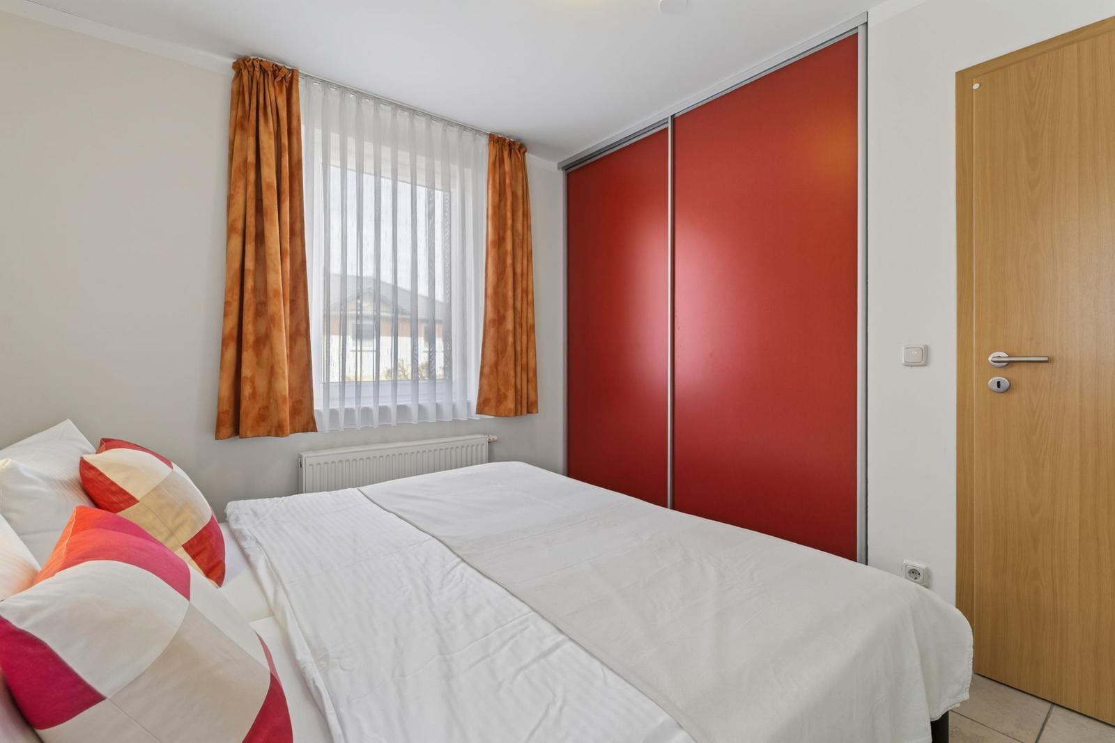 Schlafzimmer mit Bett, rotem Schrank und Fenster mit Vorhängen.
