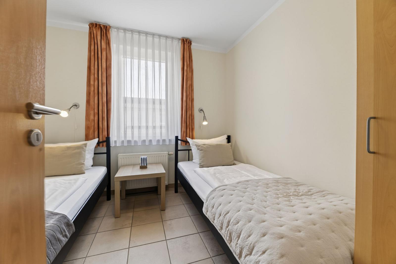 Zwei Einzelbetten mit Tisch und Fenster im Zimmer.