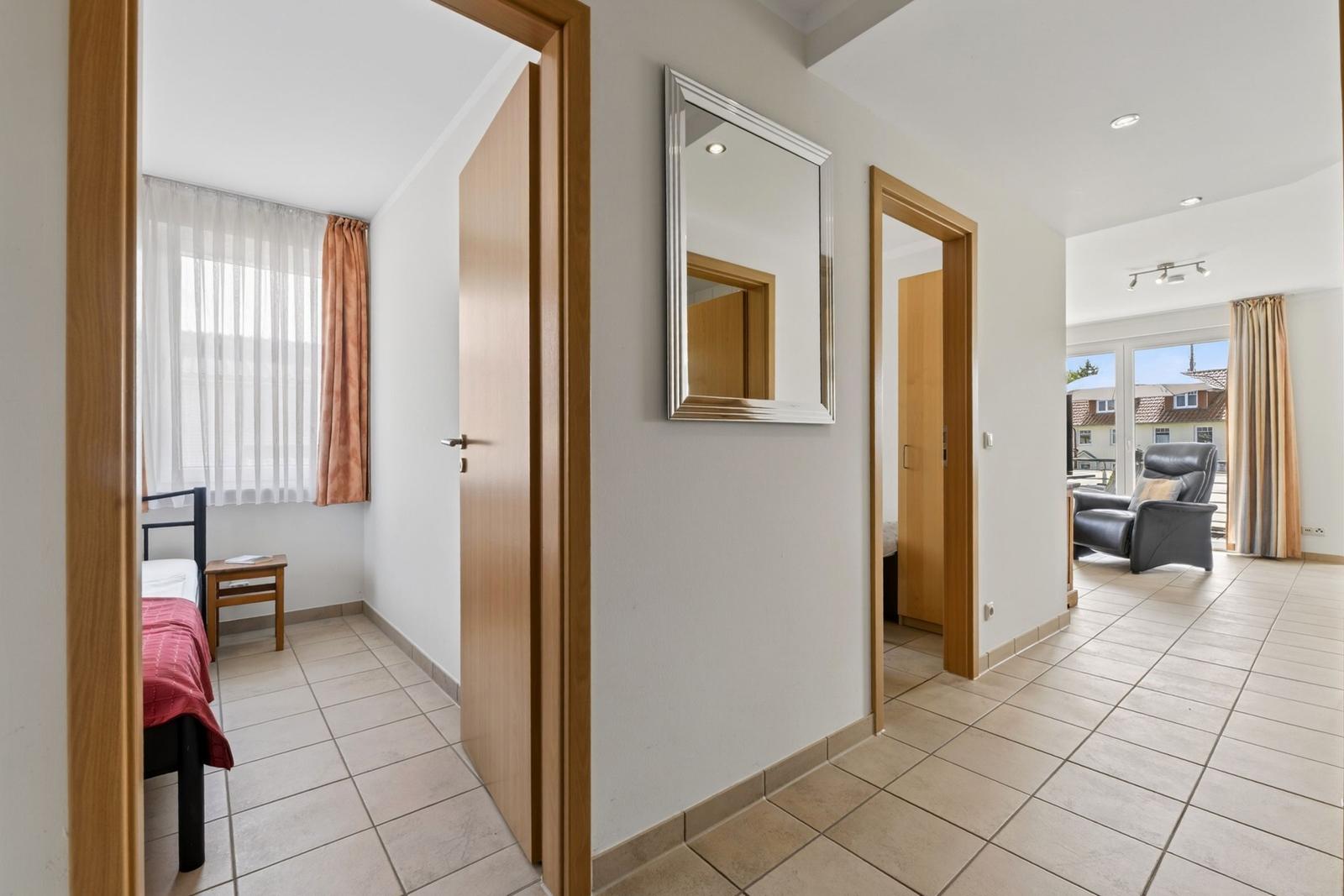 Flur mit Spiegel, Schlafzimmer und Wohnbereich mit Sessel und Blick auf Balkon.