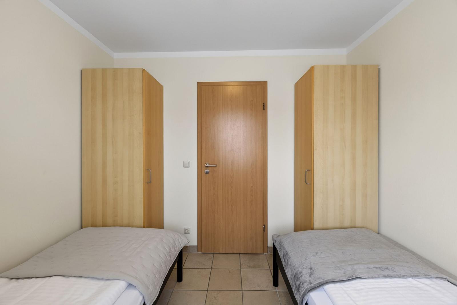 Zwei Einzelbetten mit Holzschränken und Tür im Hintergrund.