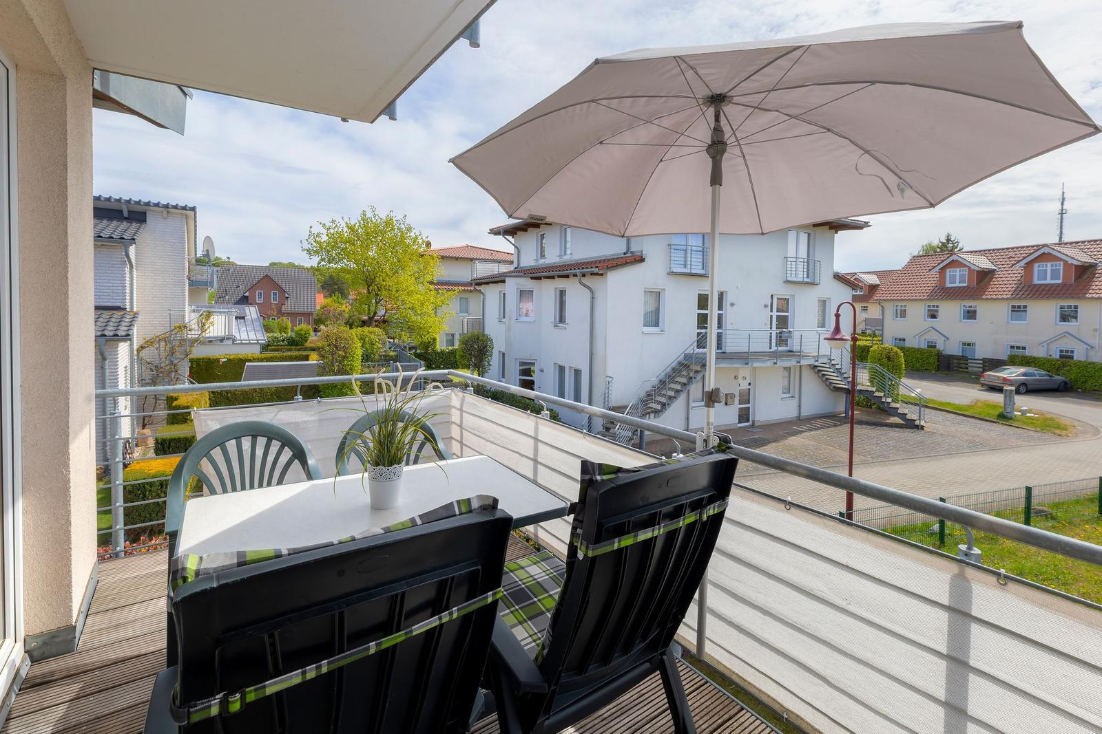 Terrasse mit Tisch, Stühlen und Sonnenschirm. Blick auf Wohnhäuser und Grünflächen.