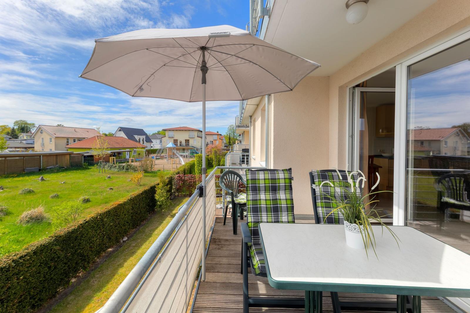 Terrasse mit Tisch, Stühlen und Sonnenschirm. Blick auf Garten und Nachbarhäuser.