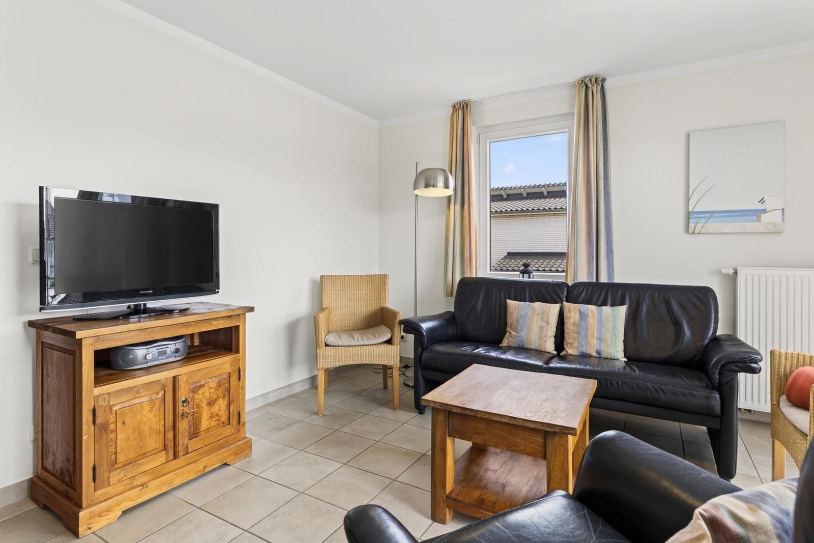 Wohnzimmer mit Sofa, Fernseher und Fenster