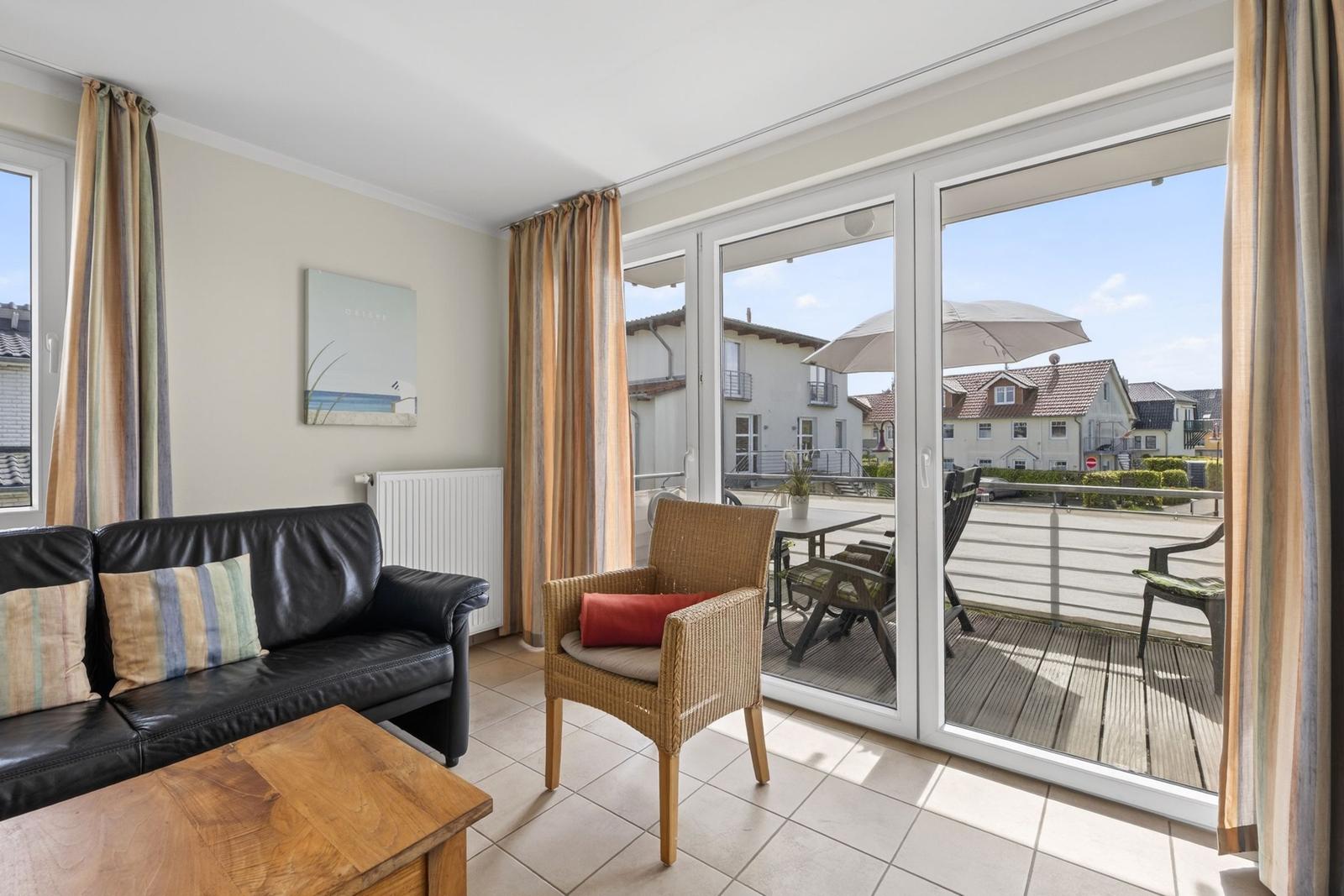 Wohnzimmer mit Sofa, Stuhl und Balkon mit Tisch und Sonnenschirm.