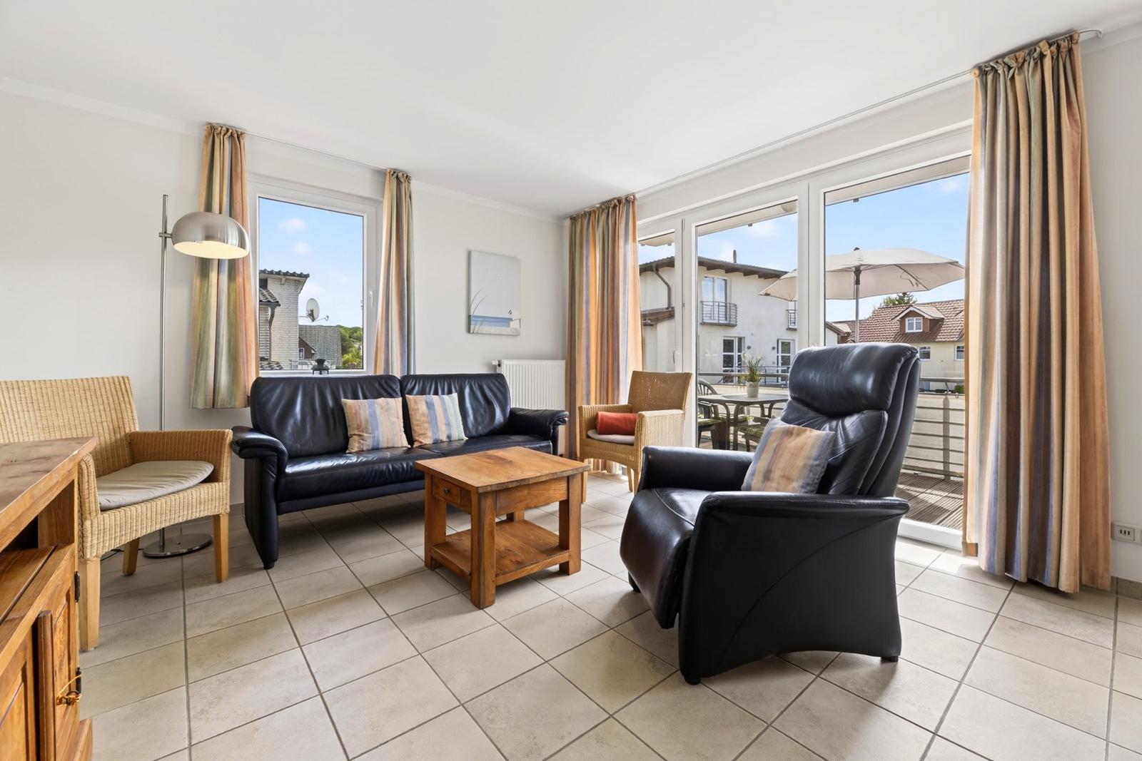 Wohnzimmer mit Ledersofa, Sessel und Terrasse. Holztisch und Gardinen.