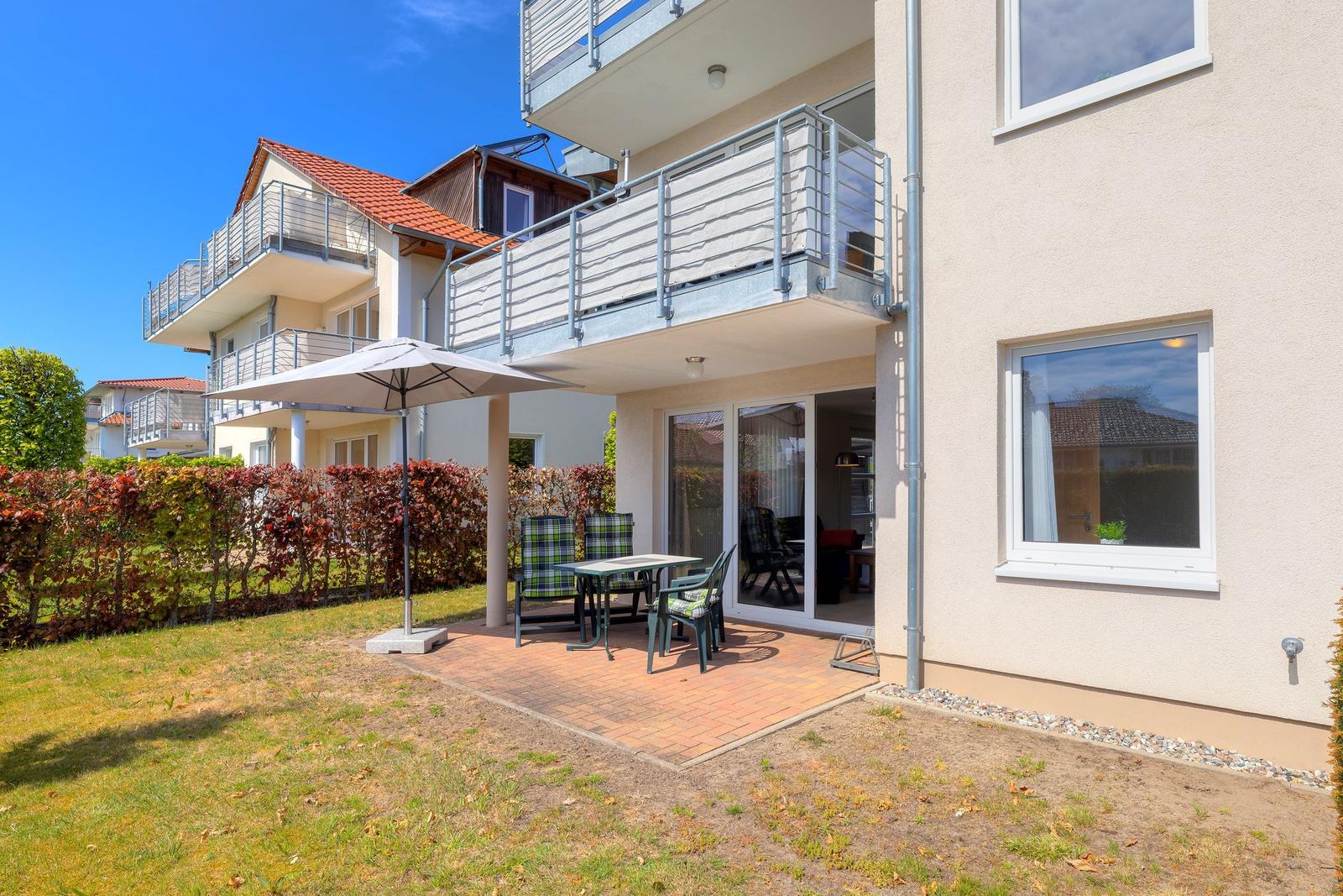 Terrasse mit Tisch, Stühlen und Sonnenschirm. Hinterhof mit Rasen und Hecke.