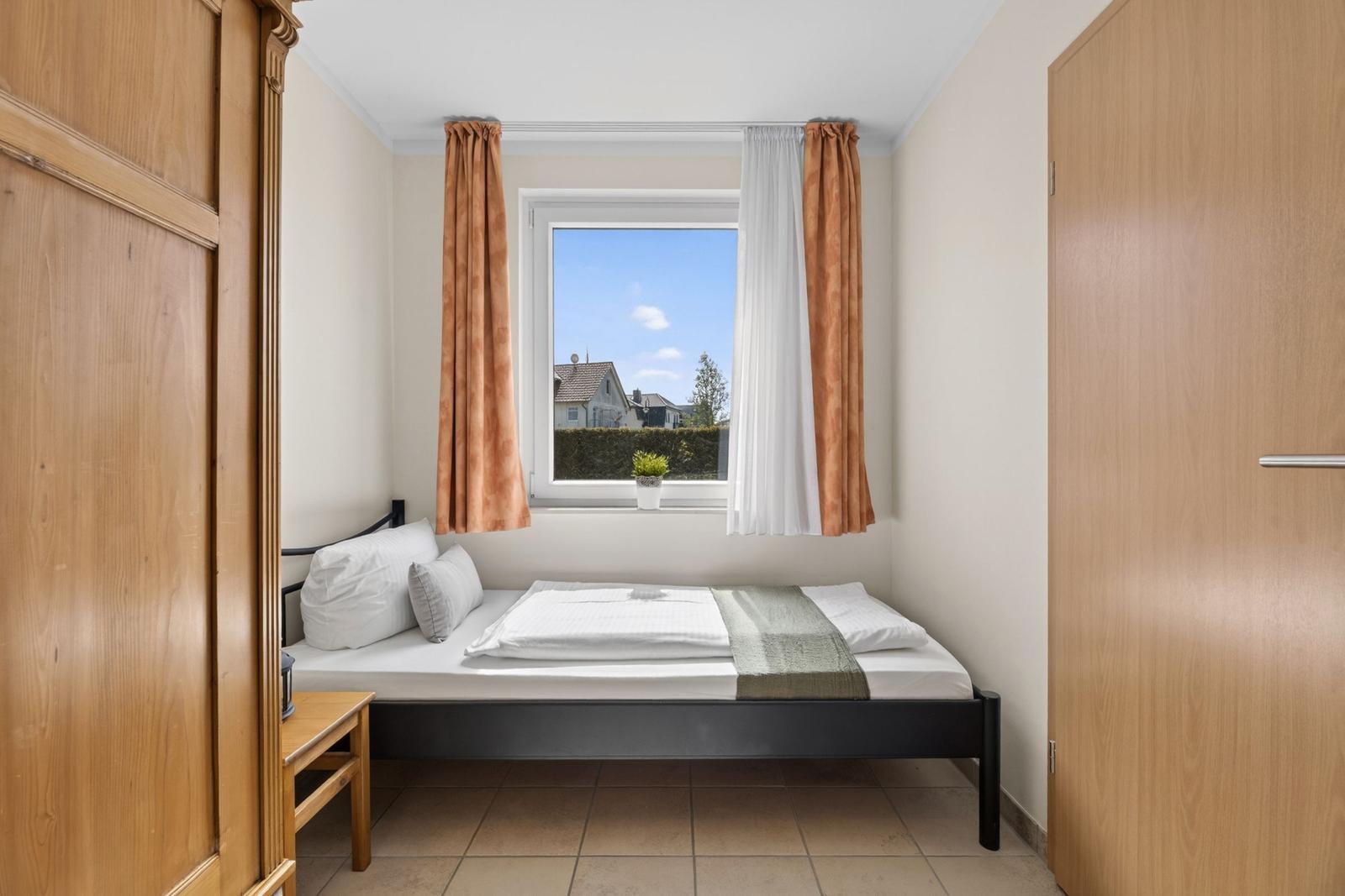 Schlafzimmer mit Bett, Fenster und Holzmöbeln.