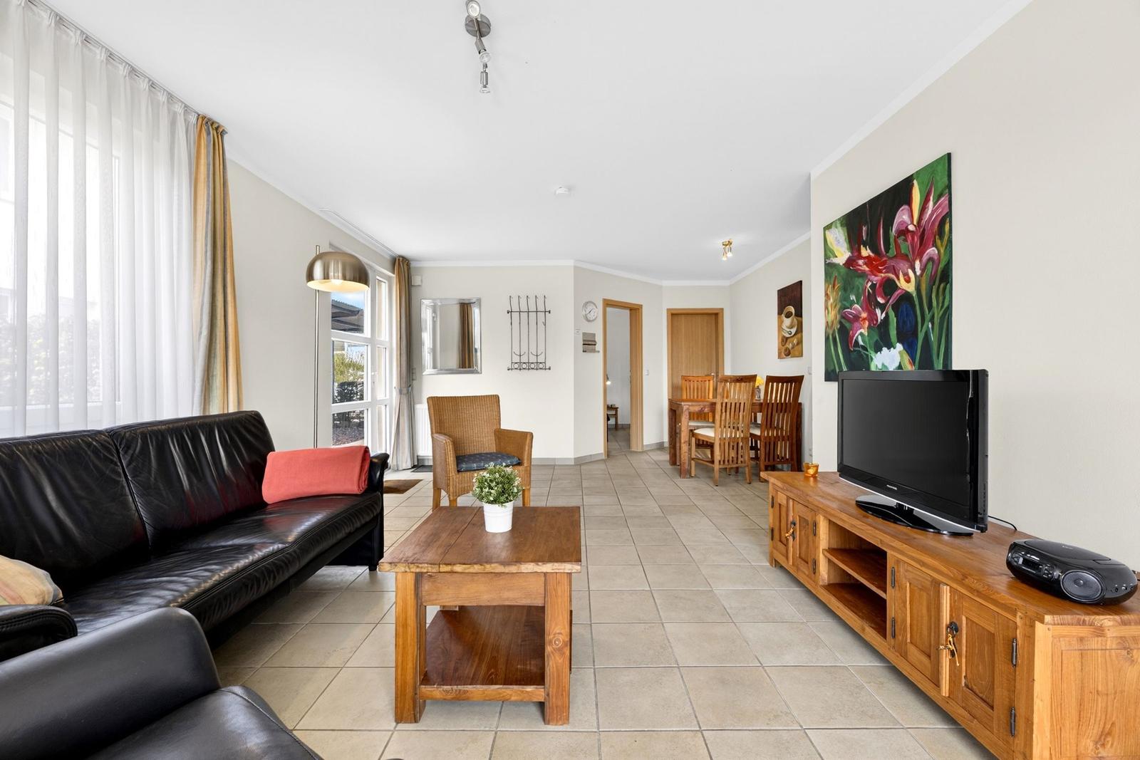 Wohnzimmer mit Sofa, Couchtisch und Fernseher. Essbereich mit Holztisch und Stühlen.