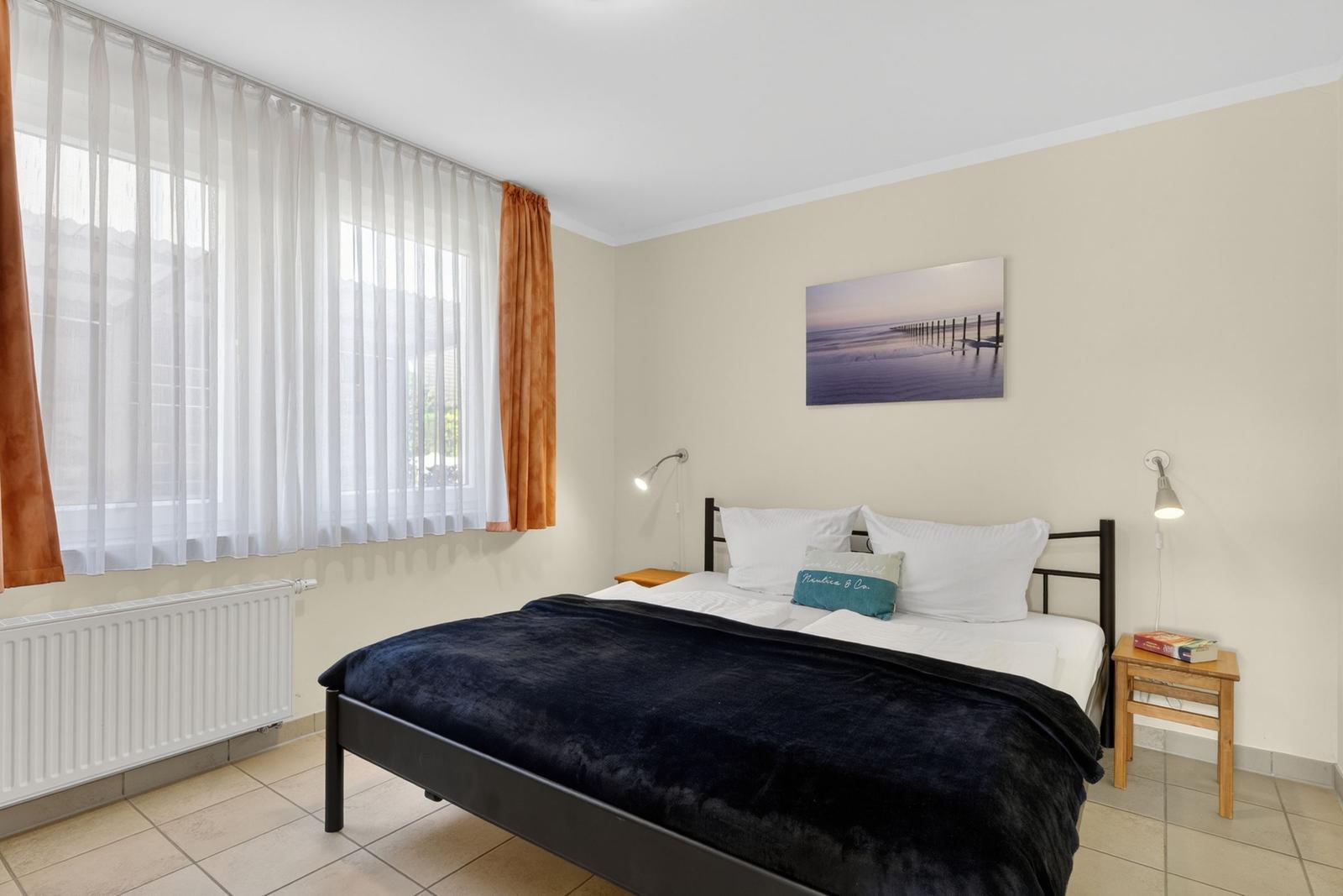 Schlafzimmer mit Bett, Wandbild und Fenster mit Vorhängen.