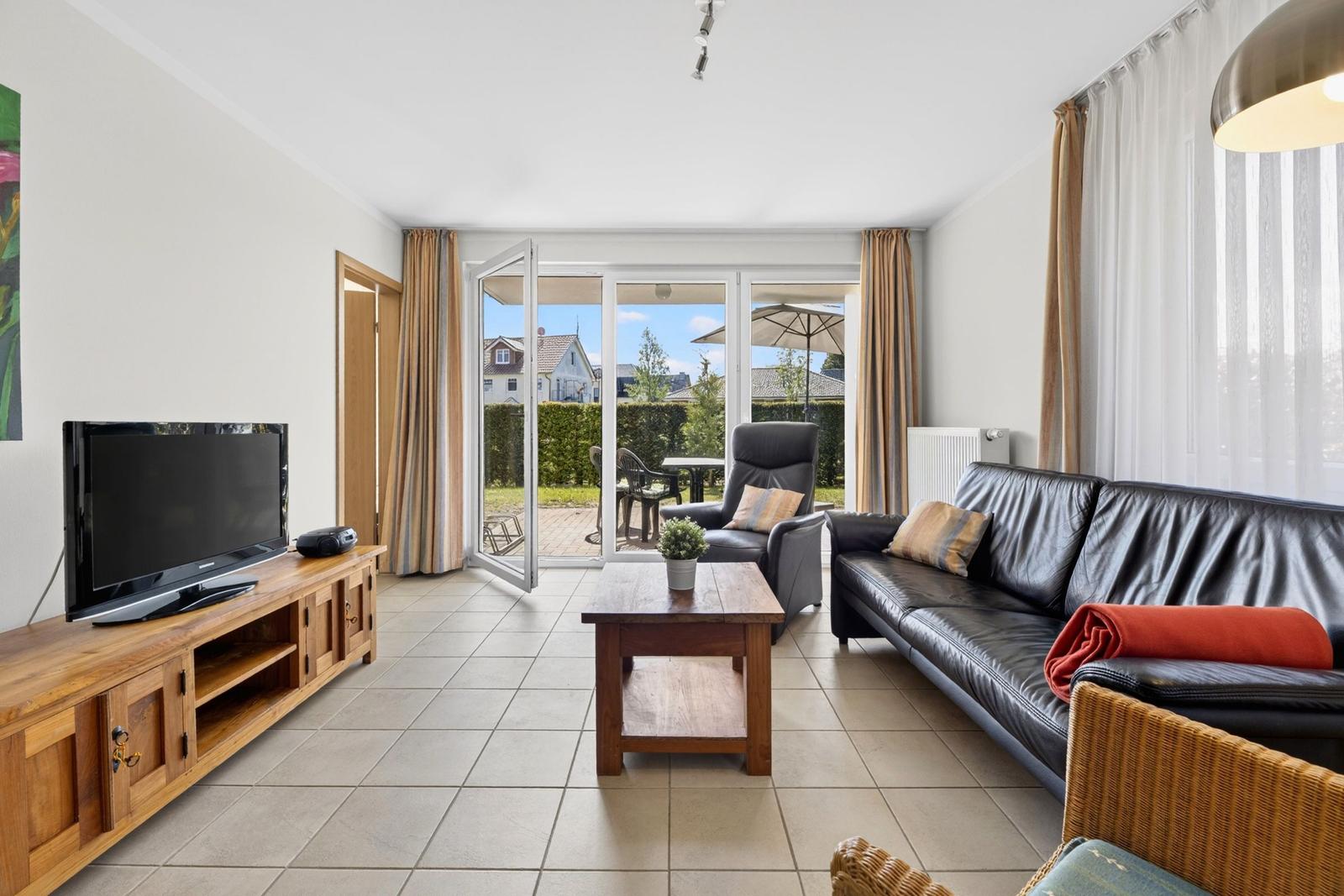 Wohnzimmer mit Sofa, Fernseher und Terrasse mit Blick auf Garten.