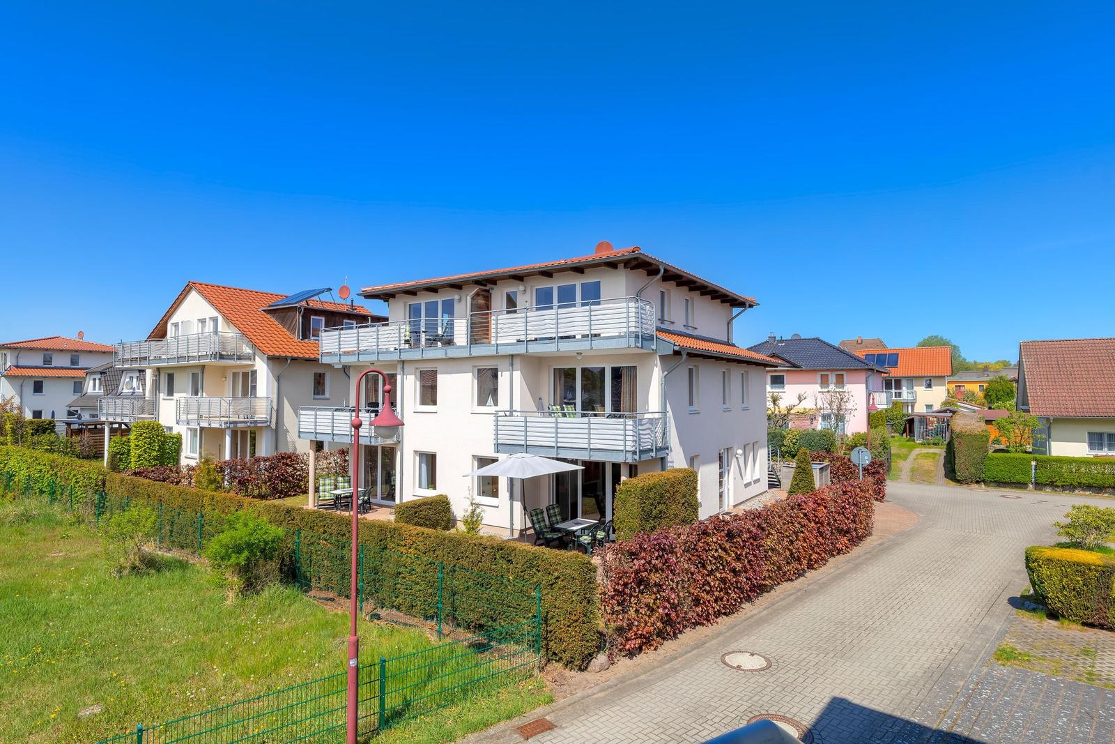 Ferienhaus mit Balkonen und Gartenbereich unter blauem Himmel.