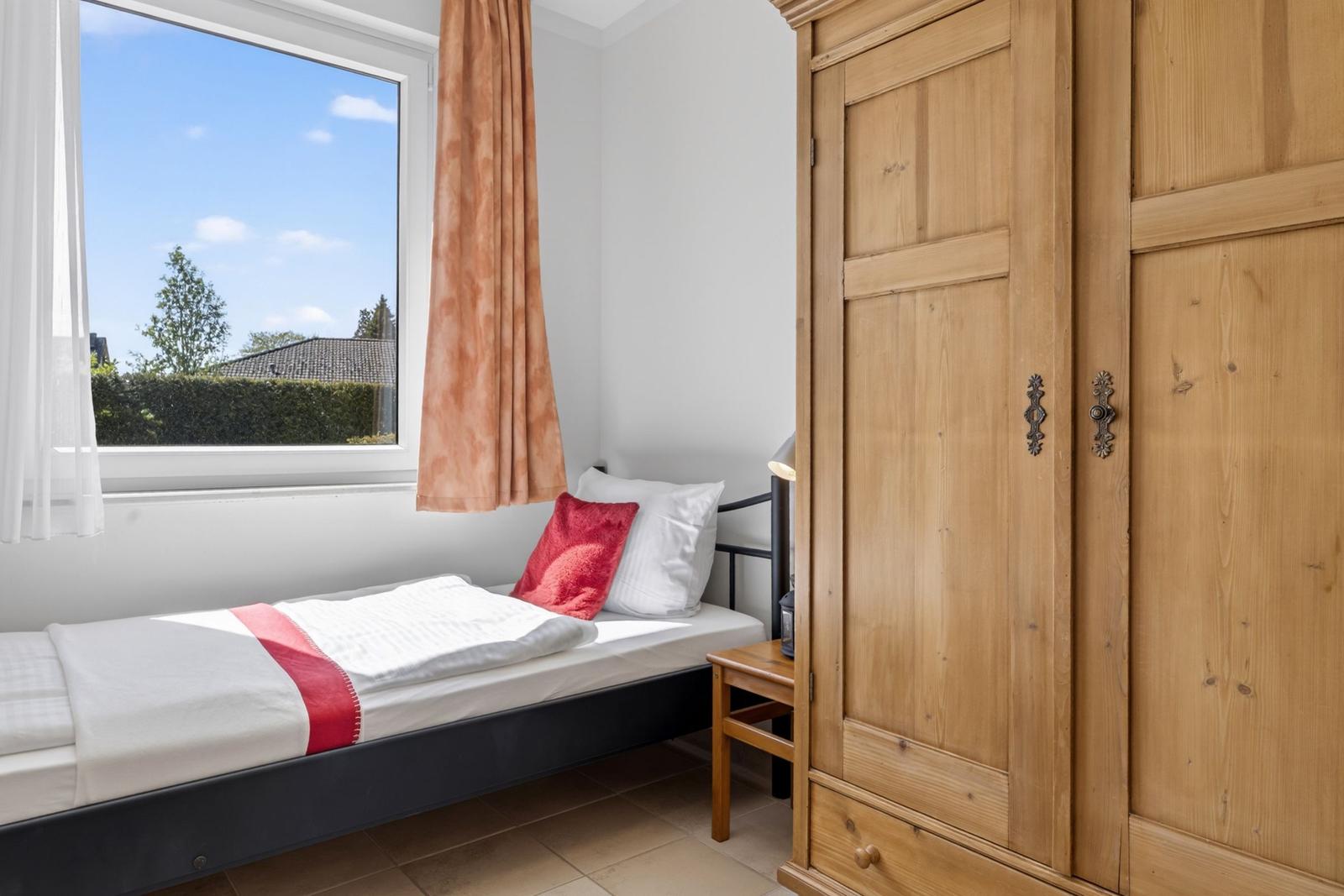 Ein Schlafzimmer mit Bett, Holzschrank und Fenster mit Blick auf Garten.