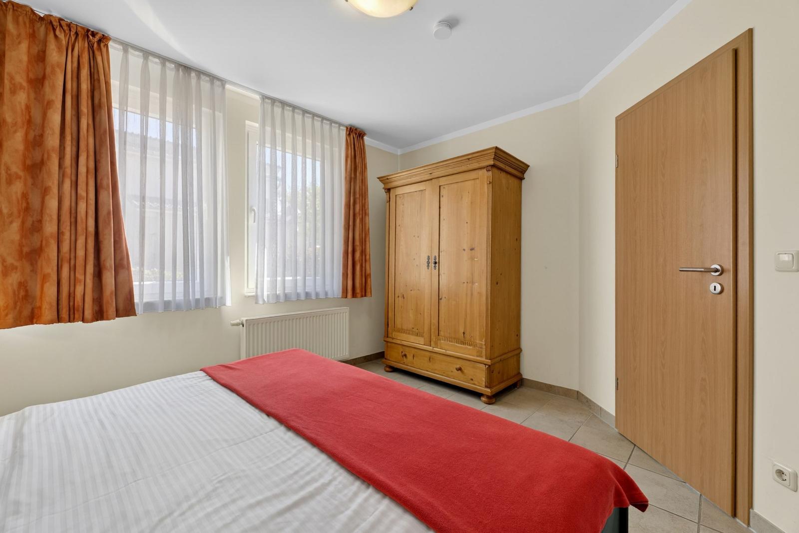Schlafzimmer mit Bett, Holzschrank und Fenster mit Vorhängen.