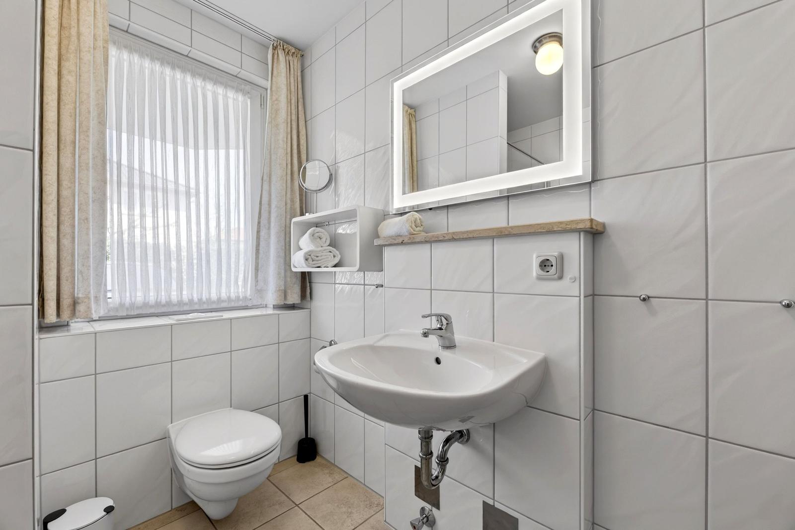 Badezimmer mit Toilette, Waschbecken und Spiegel. Fenster mit Vorhängen.