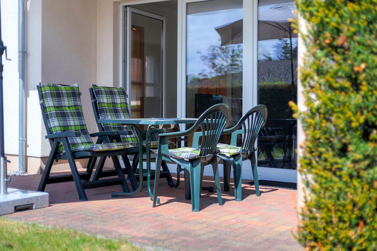 Terrasse mit Tisch und Stühlen, grüne Kissen, Glasfront zur Wohnung