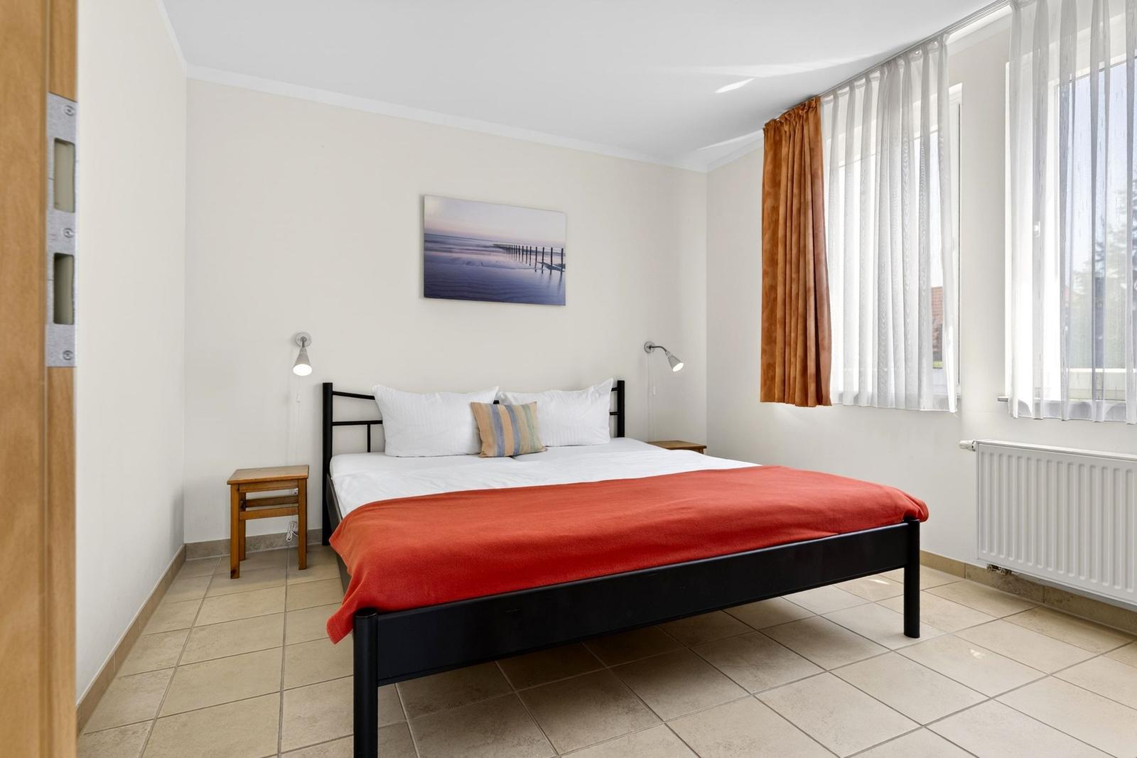 Schlafzimmer mit Doppelbett, Wandbild und Fenster mit Vorhängen.