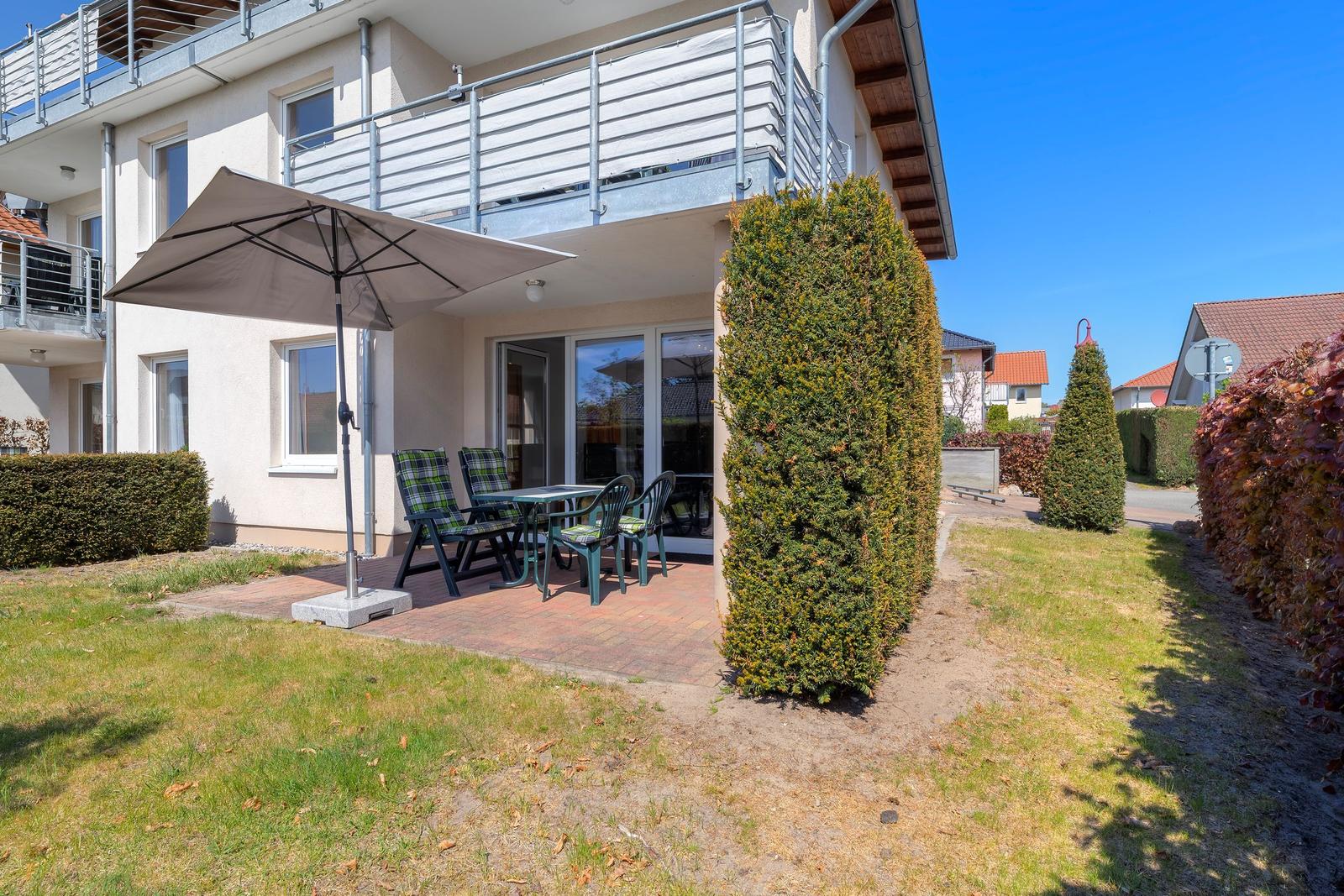 Terrasse mit Tisch, Stühlen und Sonnenschirm vor einem Haus mit Balkon.
