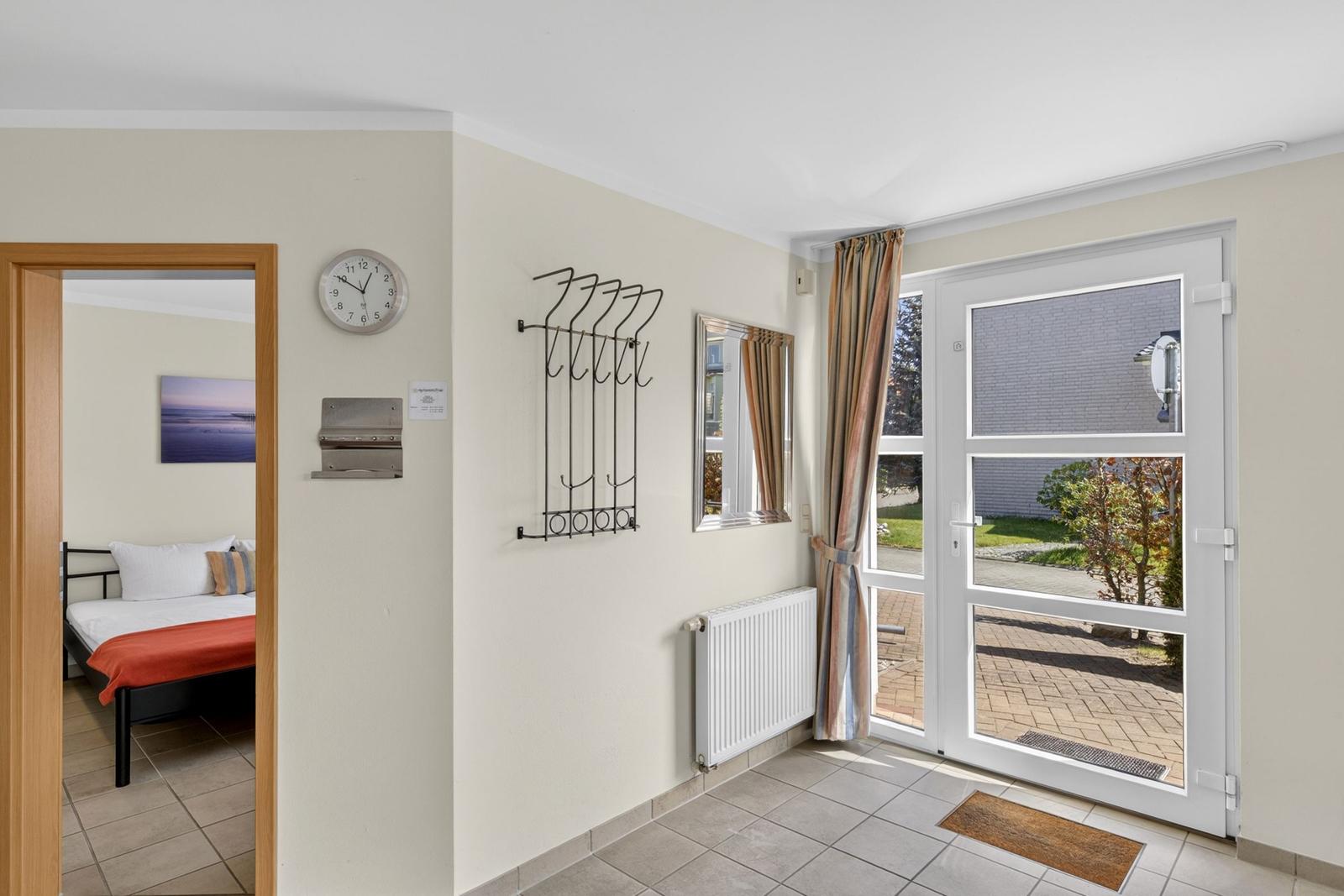 Eingangsbereich mit Tür zum Garten und Blick in Schlafzimmer mit Bett und Wandbild.