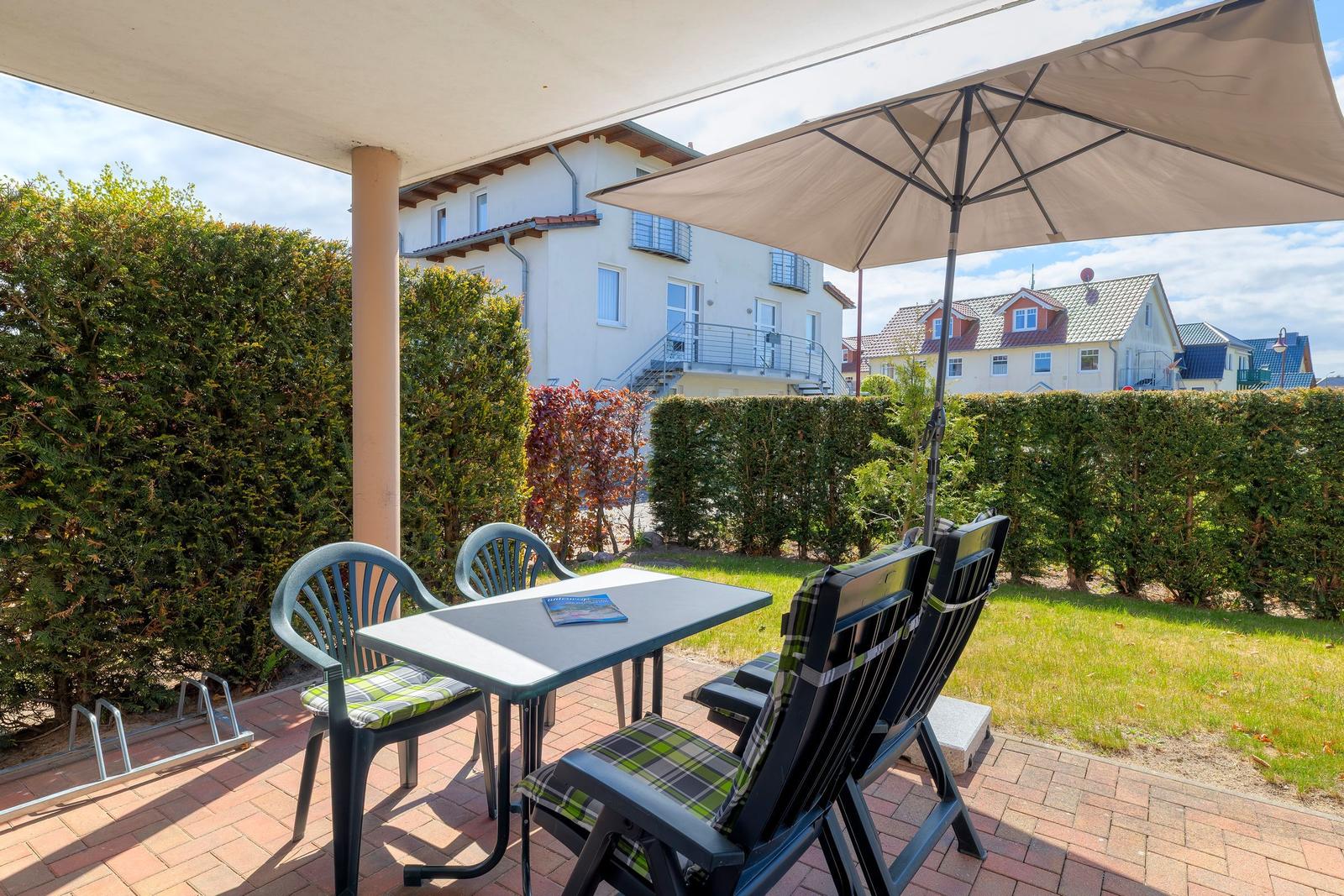 Terrasse mit Tisch, Stühlen und Sonnenschirm. Hinterhof mit Rasen und Hecke.