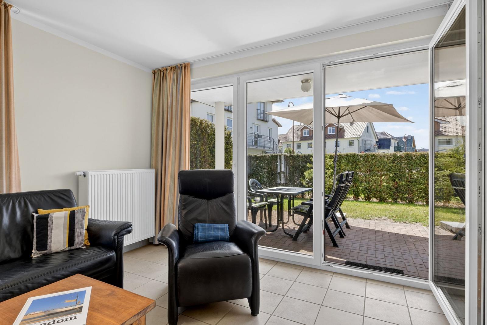 Wohnzimmer mit Sitzgelegenheiten und Blick auf den Balkon mit Tisch und Stühlen.