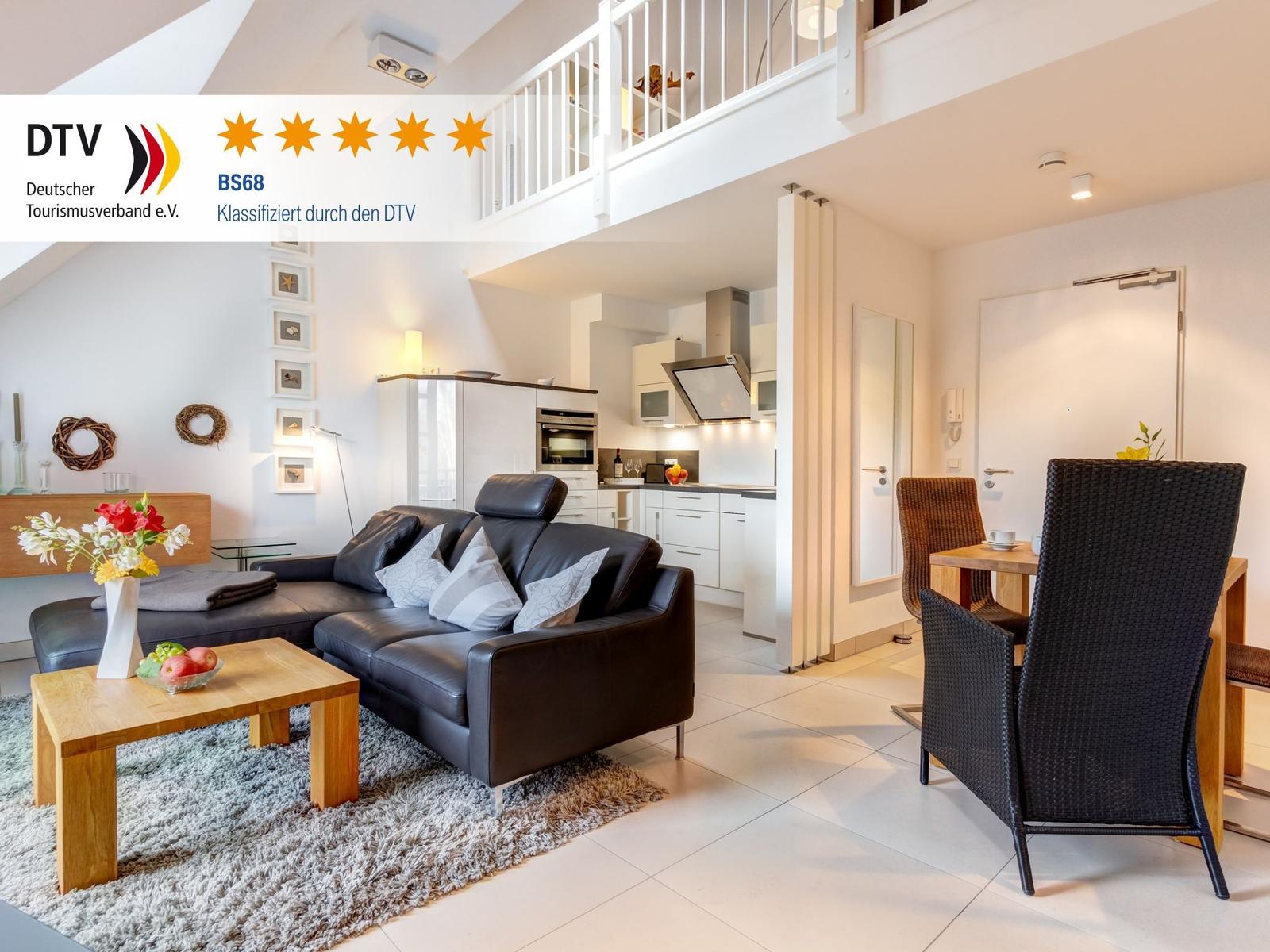 Wohnzimmer mit Sofa, Esstisch und Küche unter einer Galerie.